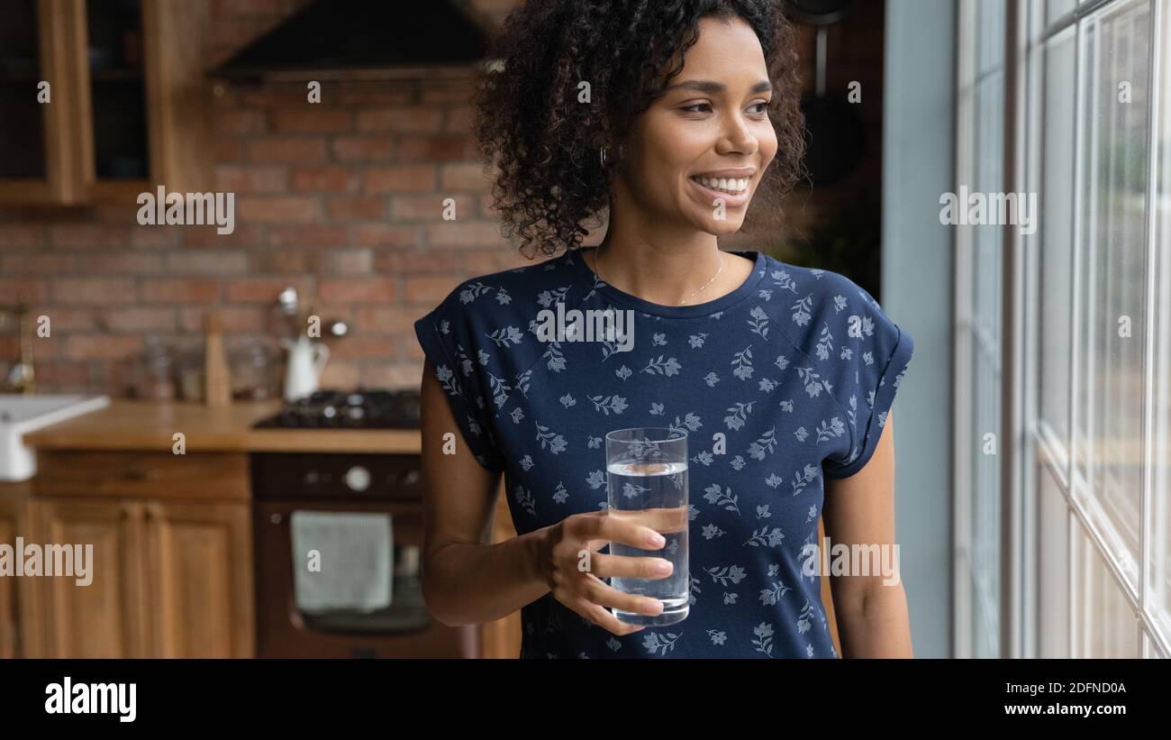 Verträumte junge afroamerikanische Frau mit einem Glas Wasser. Stockfoto