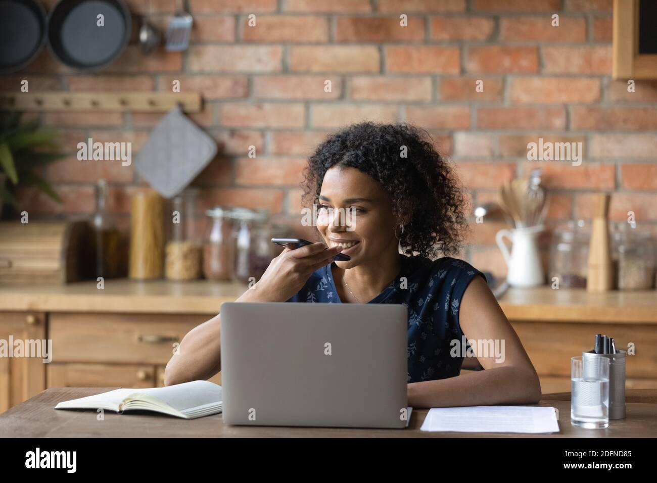 Lächelnde junge Mischling Frau diktiert Audio-Nachricht. Stockfoto