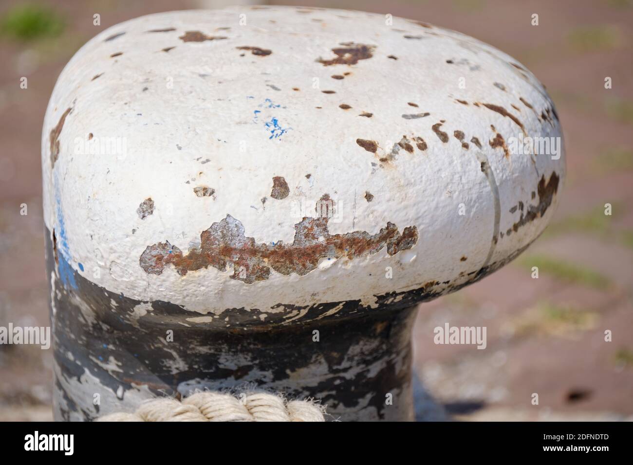 Abstrakte Hintergrund Textur von weißen rostigen Poller. Ein dickes starkes Seil liegt auf dem Boden neben dem Poller. Stockfoto