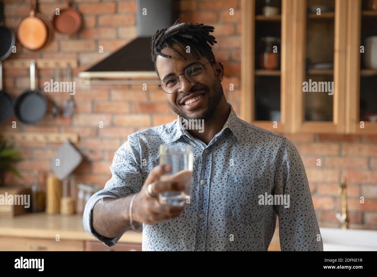 Lächelnder junger afroamerikanischer Mann schlägt ein Glas Wasser vor. Stockfoto