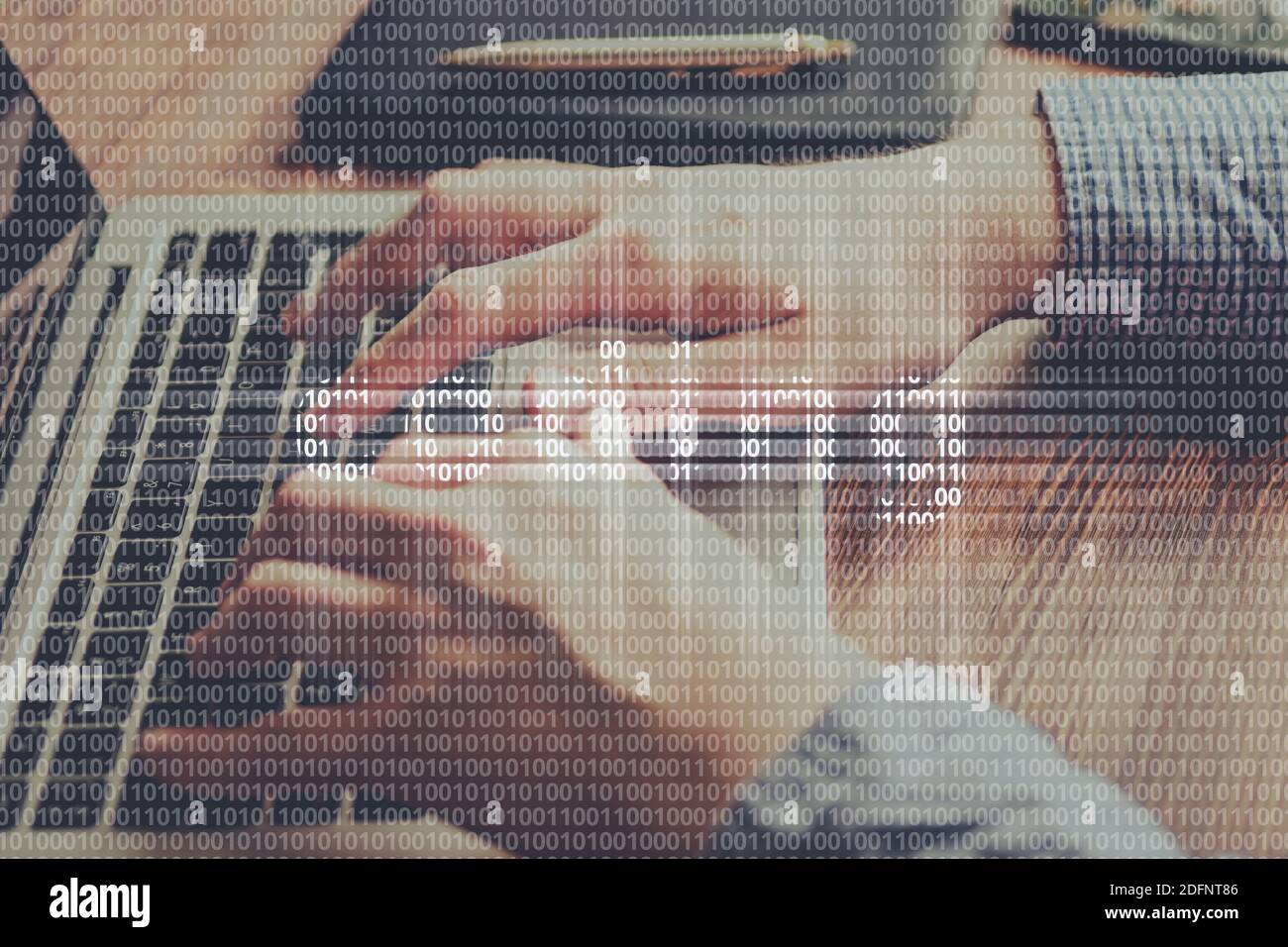 Das Konzept der Codierung aus einem Binärcode auf dem Hintergrund einer Person, die auf einem Laptop tippen. Stockfoto