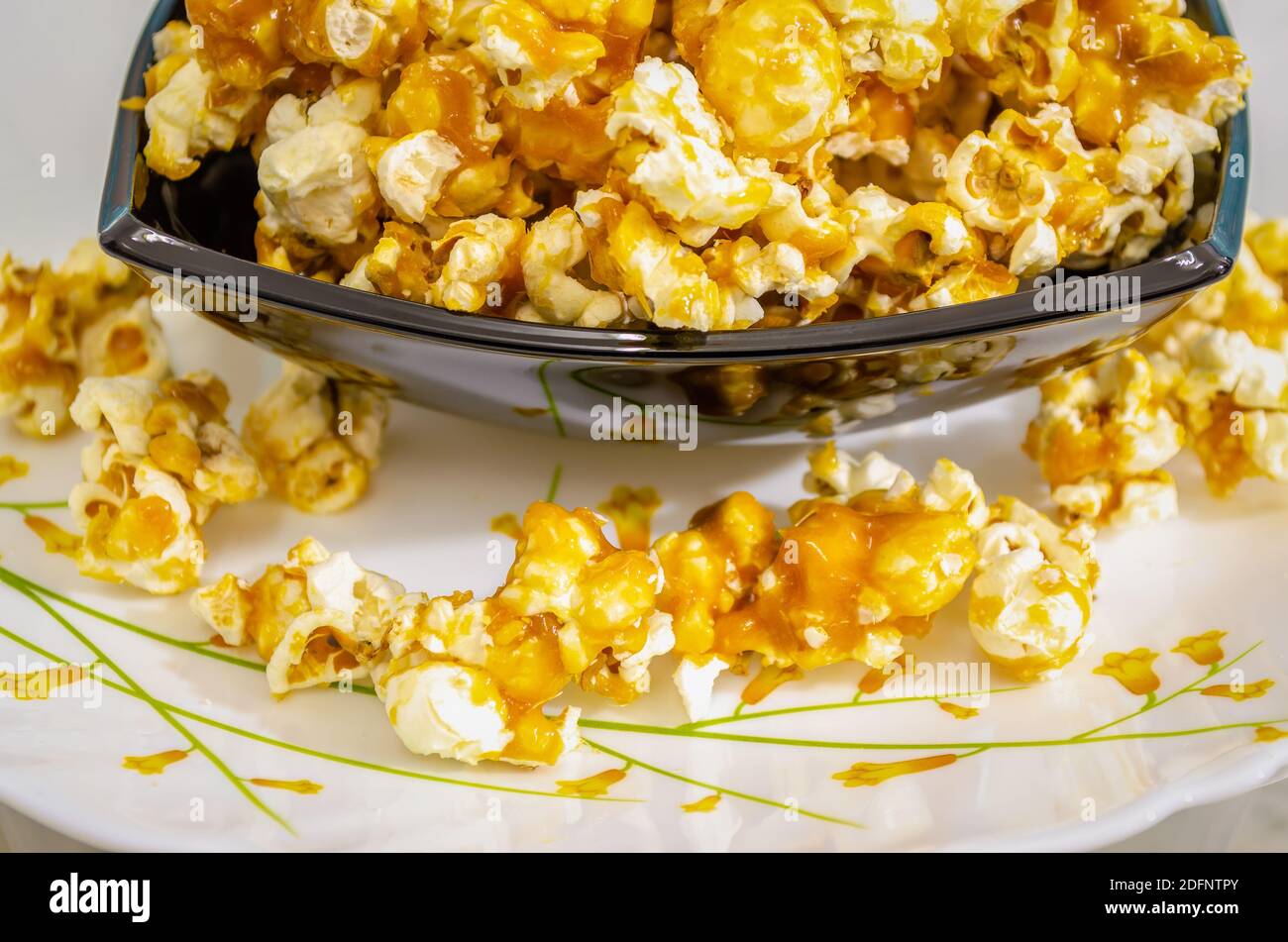 Nahaufnahme von süßem und Crunchy Caramel Popcorn in einer Schüssel Und verschüttet auf eine Platte darunter Stockfoto