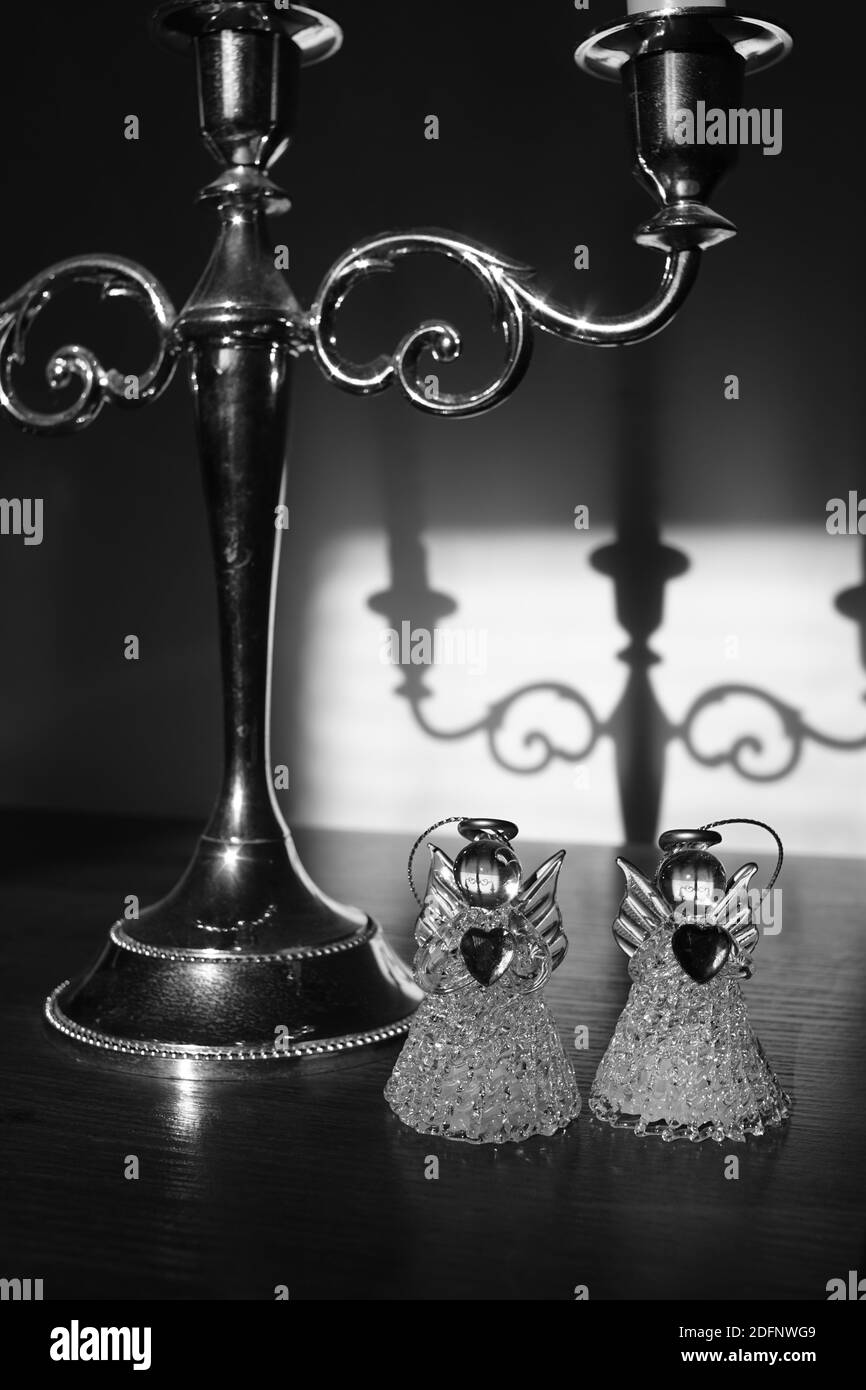 Zwei kleine Engelstatuen und ein Vintage-Kerzenständer auf dem Tisch. Schattenspiegelung an der Wand. Schwarzweiß-Foto Stockfoto