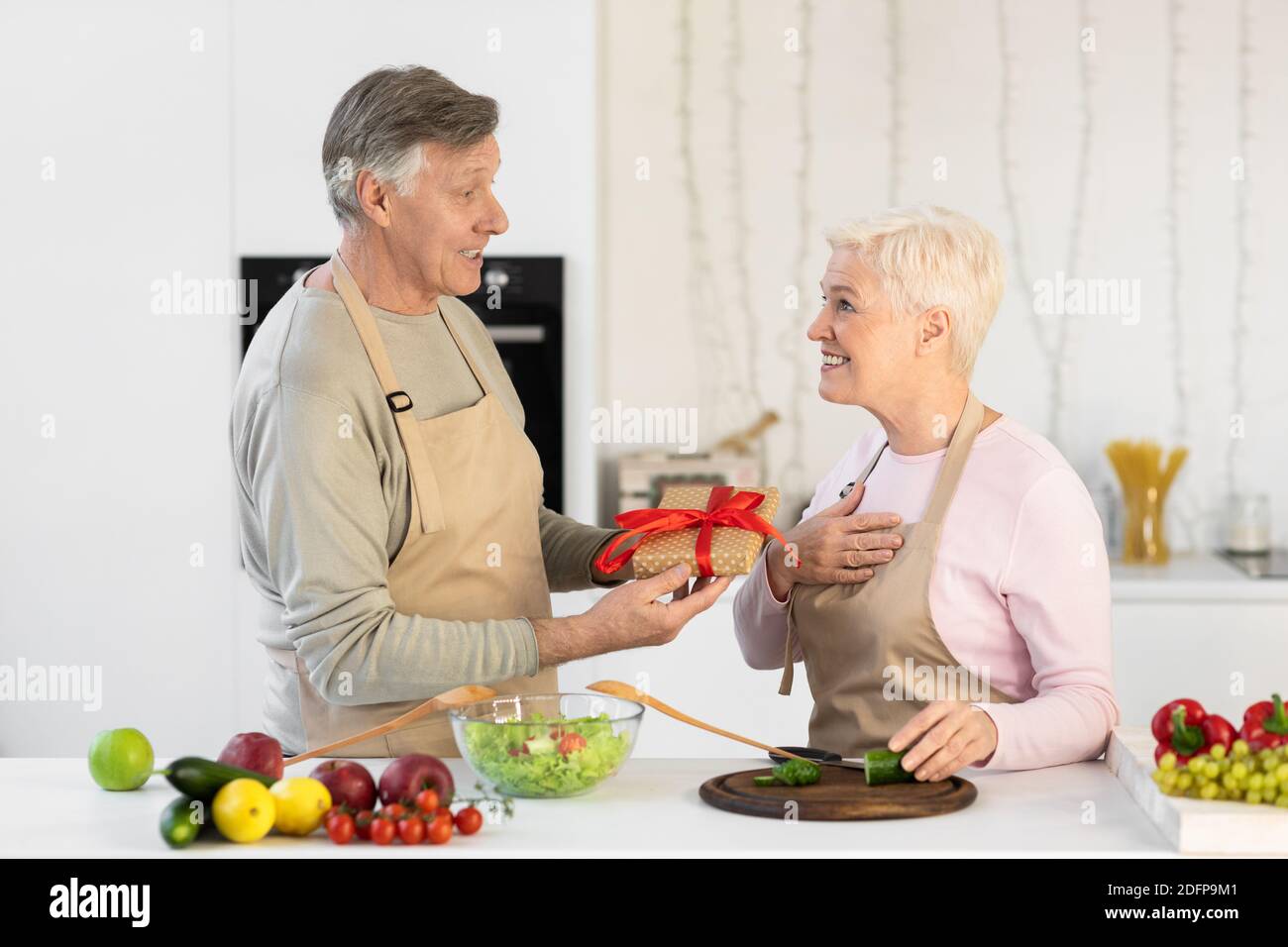 Ehemann Im Alter, Der Frau In Der Küche Zu Hause Ein Geschenk Gibt Stockfoto