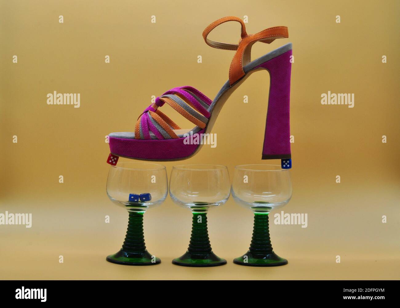 Komposition mit weiblichem Schuh auf Würfel auf Brille ausbalanciert. Konzeptionelles Foto über die Gefahren des Glücksspiels. Stockfoto