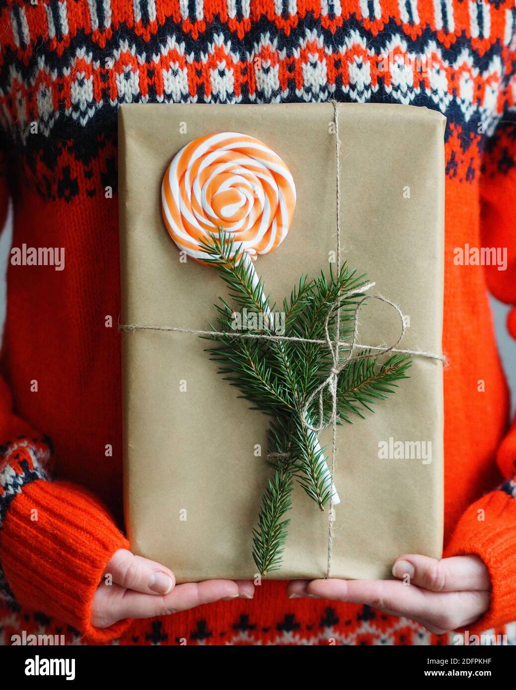 Frau mit modernem Weihnachtsgeschenk. Geschenk in braunem Papier mit Kiefernästen und Lollipop befestigt eingewickelt. Stockfoto