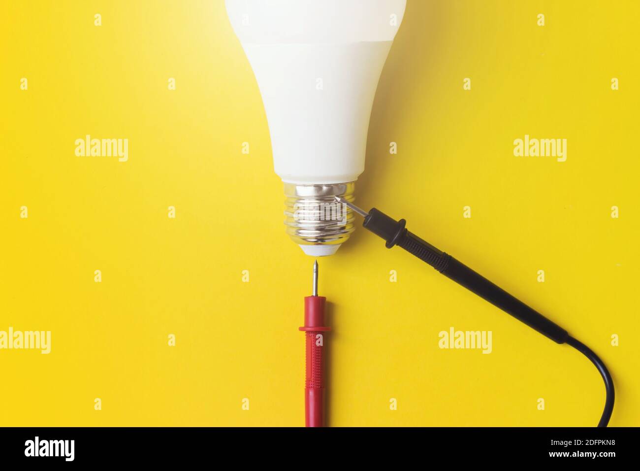 Vitalenergie-Konzept. Glühlampe mit Multimetersonden auf gelbem Hintergrund. Technologiekonzept. Draufsicht, flach liegend Stockfoto