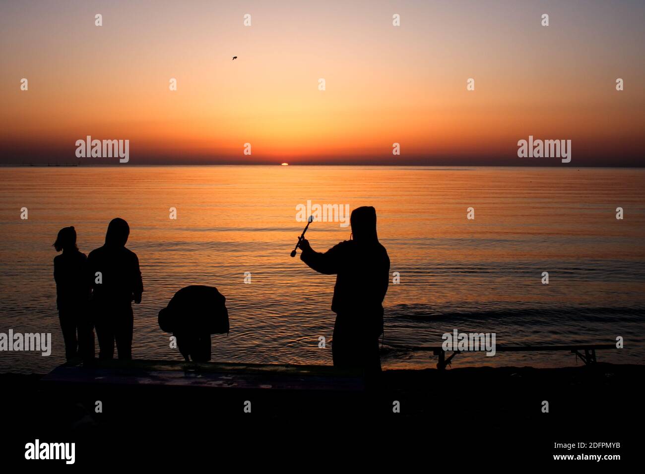 Die Menschen werden am Strand während eines Sommersonnenaufgangs silhouettiert. Stockfoto