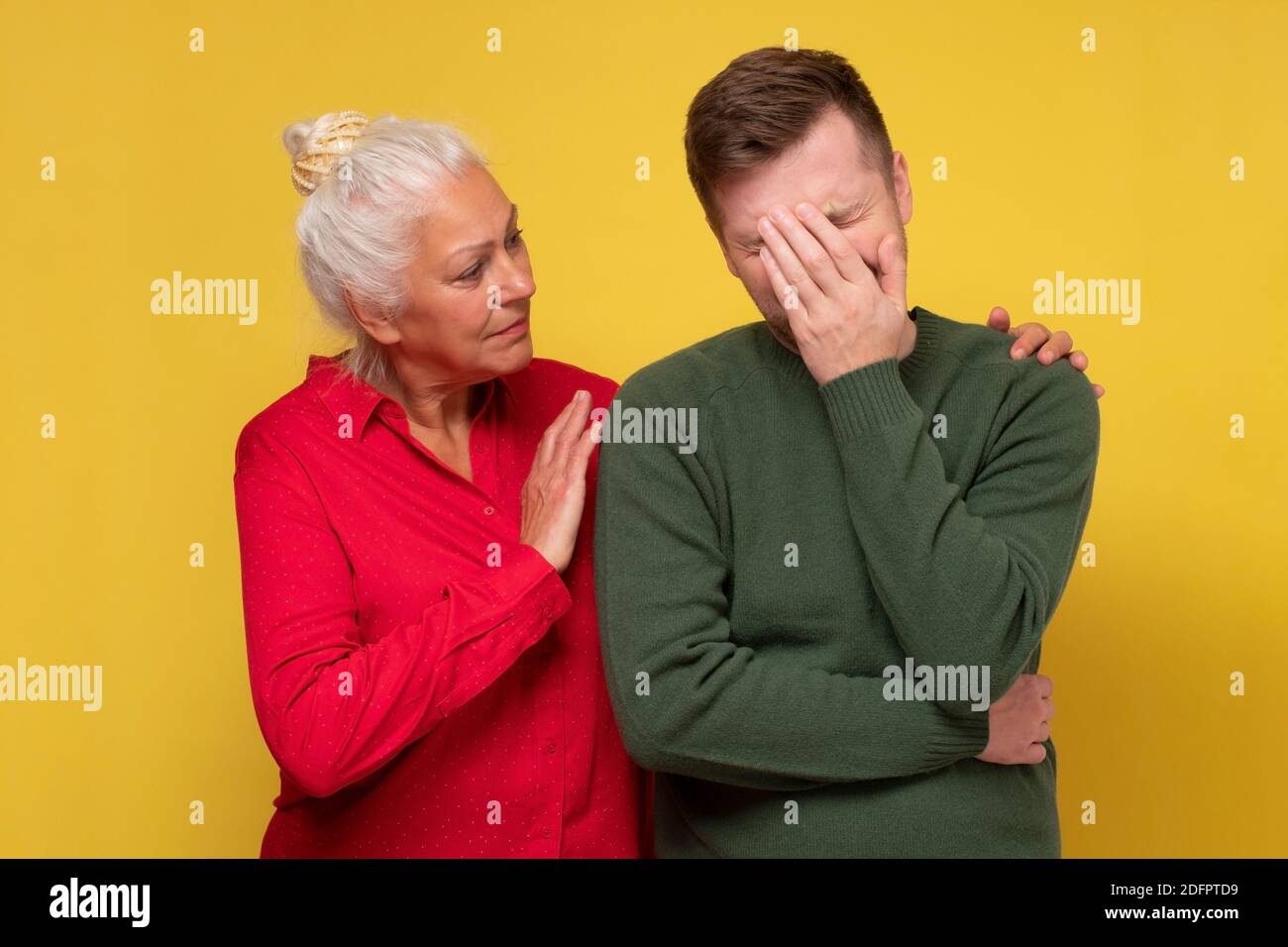 Reife Mutter hört auf ihren Sohn Probleme. Er weint. Studio auf gelber Wand. Stockfoto