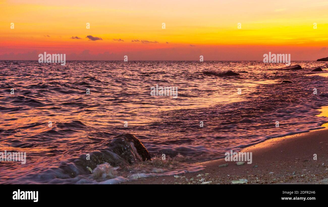 Wunderschöne Himmelsfarben nach Sonnenuntergang, glänzende Meerwasserwellen, Orange- und Gelbtöne, violettes Wasser Stockfoto