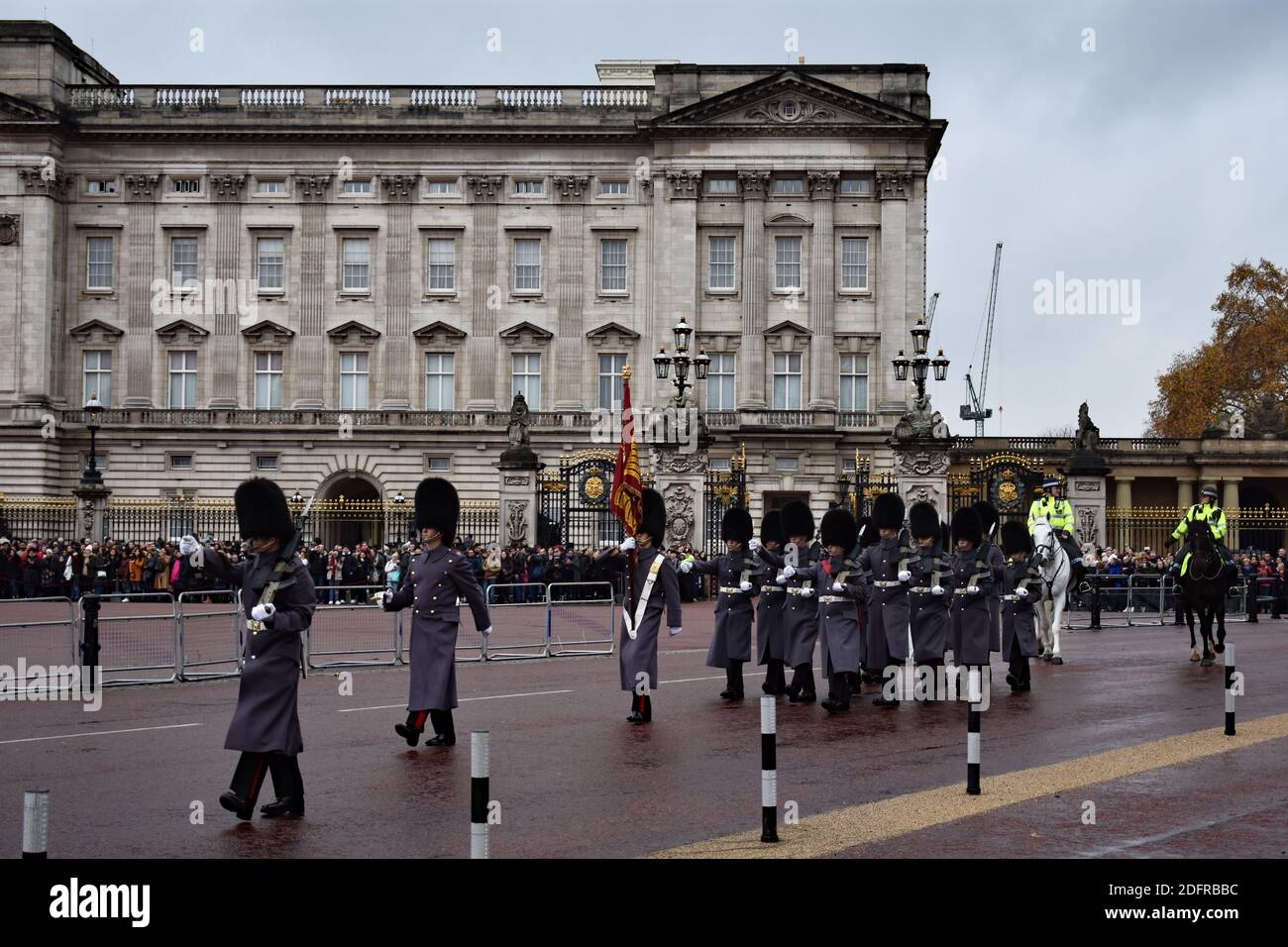 Die Wachablösung am Buckingham Palace, London. Graue Soldaten marschieren an Menschenmassen entlang der Mall vorbei, gefolgt von zwei Polizisten, die Pferde reiten. Stockfoto