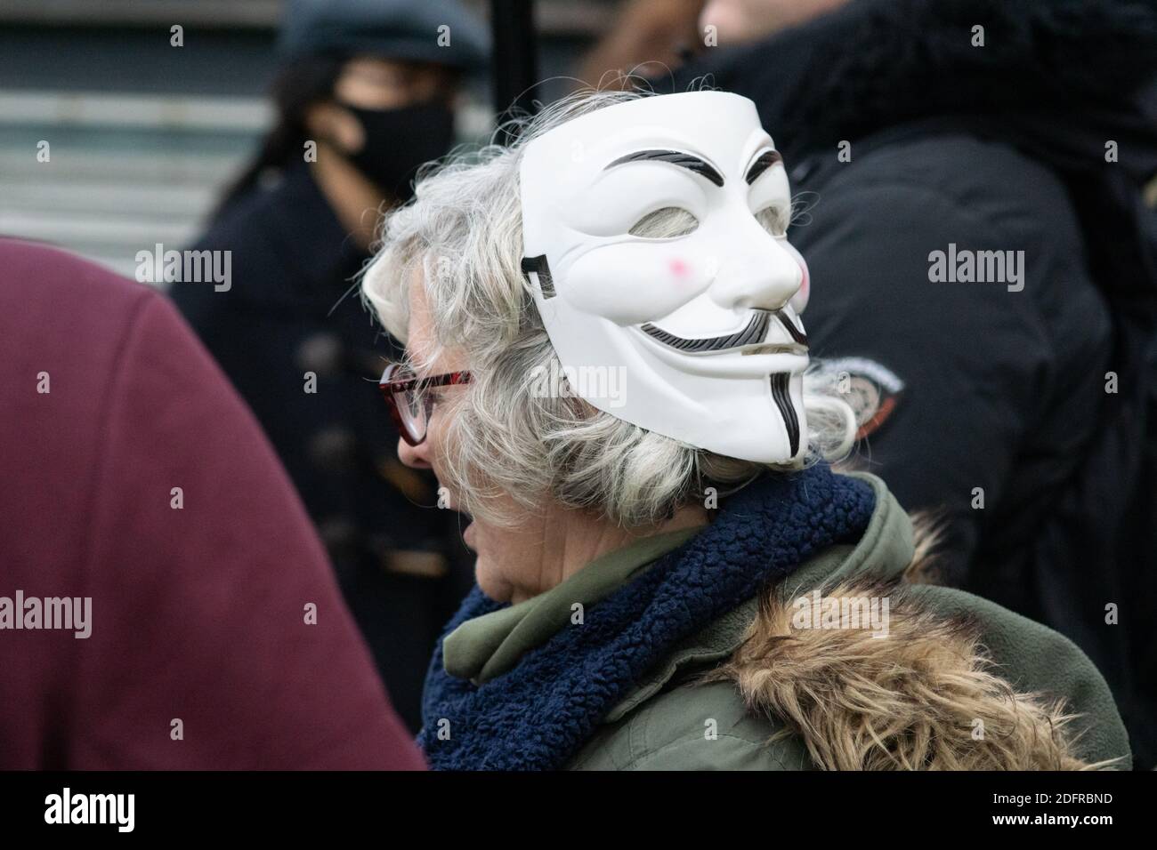 Manchester Piccadilly Gardens 6. Dez 2020: Eine grauhaarige Dame trägt eine Guy Fawkes oder Anonymous Maske auf dem Hinterkopf bei der Anti-Lockdown-Versammlung Stockfoto