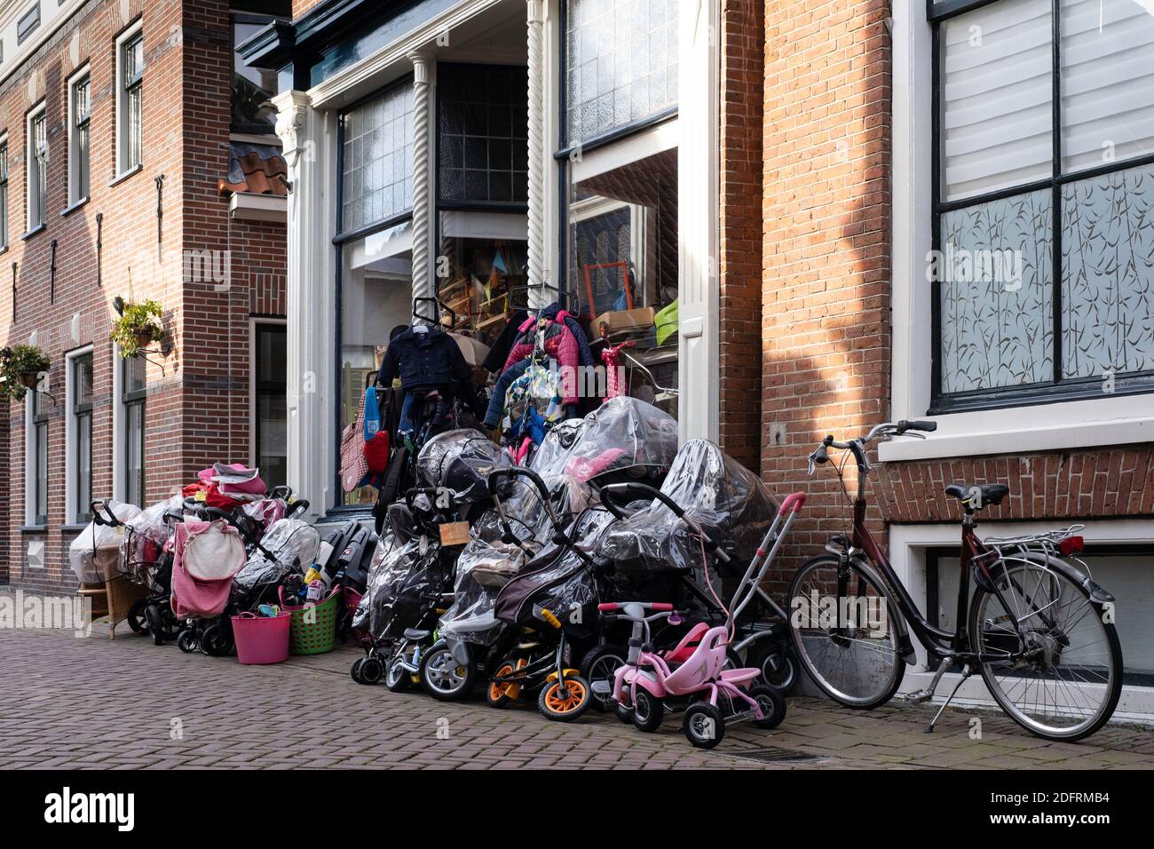 Überfüllte Ausstellung von Fahrrädern und anderen Gegenständen bei einem Verkauf vor dem Eingang und Fenster eines Ladens in Appingedam, Groningen, Niederlande Stockfoto