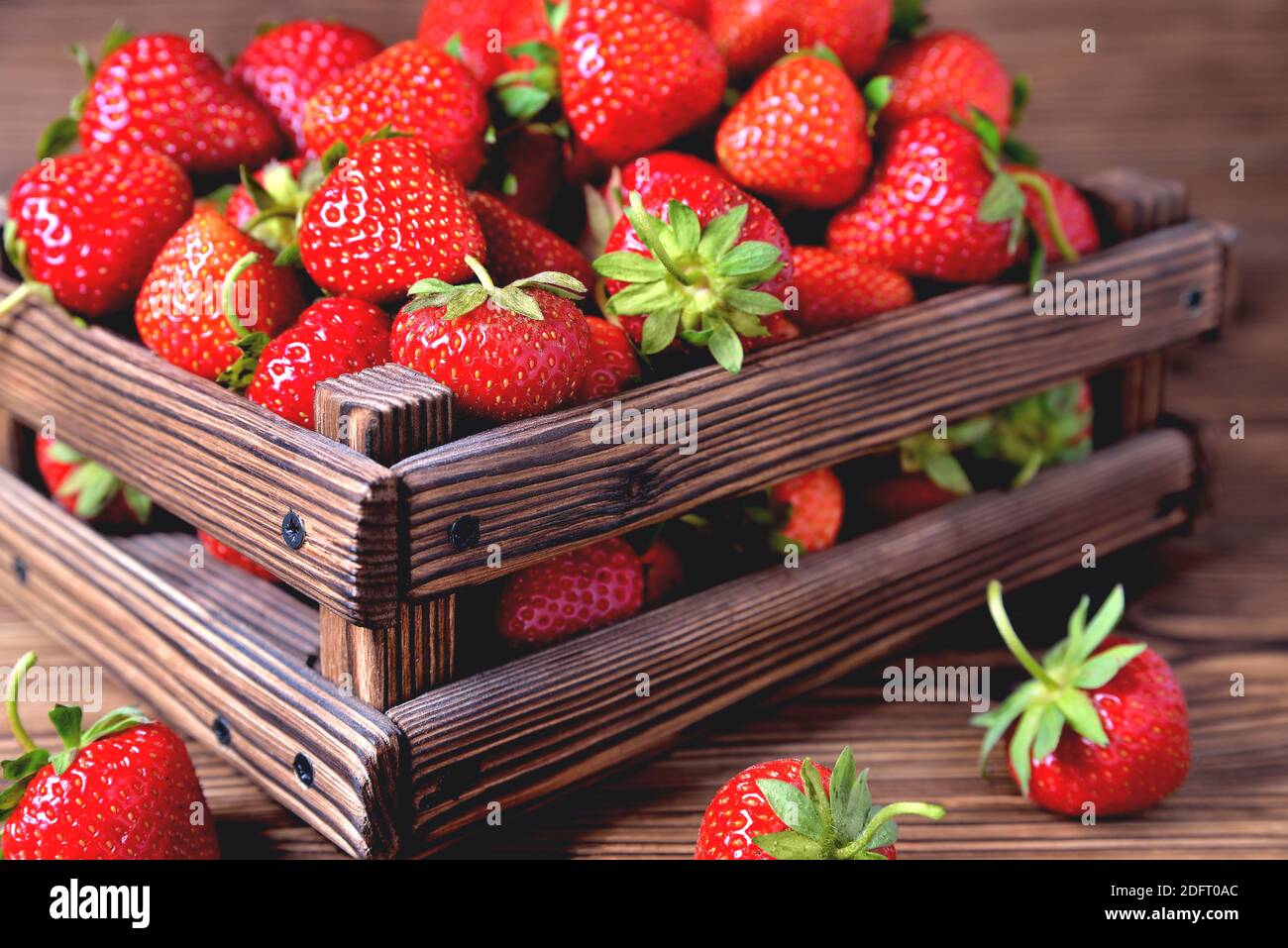 Erdbeeren in einer Holzkiste auf einem natürlichen Holzhintergrund, verschwimmen als künstlerische Technik des Autors close-up copy space Stockfoto