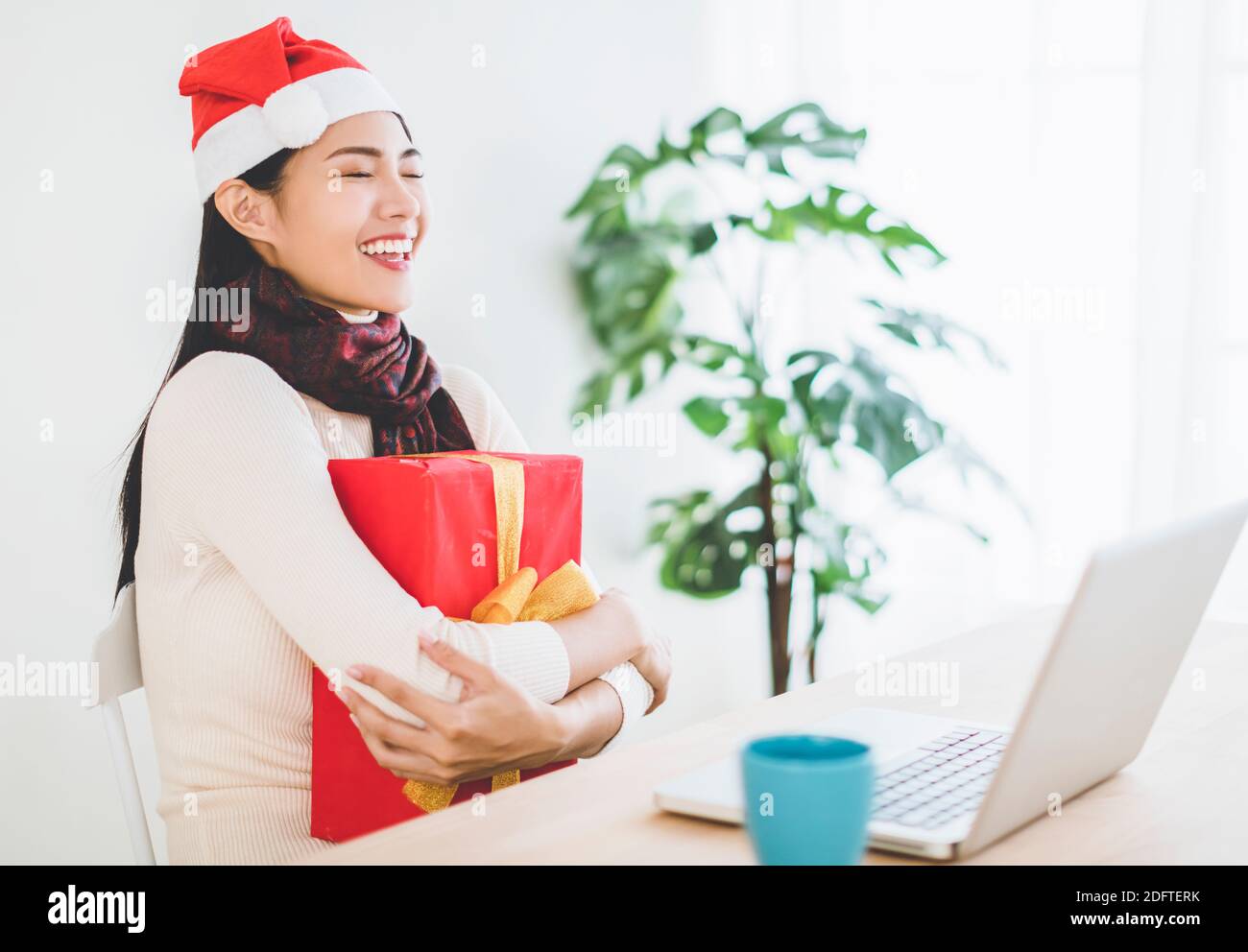 Junge Frau hält weihnachtsgeschenk in Videokonferenz mit Laptop. Weihnachten online Glückwünsche Konzept Stockfoto