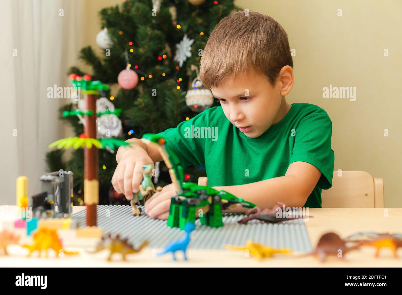 SAINT-PETERSBURG, RUSSLAND - NOVEMBER 29, 2020 Boy baute eine jurassic Welt aus Plastikblöcken und spielt mit Spielzeug Dinosaurier. Weihnachtsbaum im Hintergrund. Bleiben Sie zu Hause für Weihnachtsferien Konzept Stockfoto
