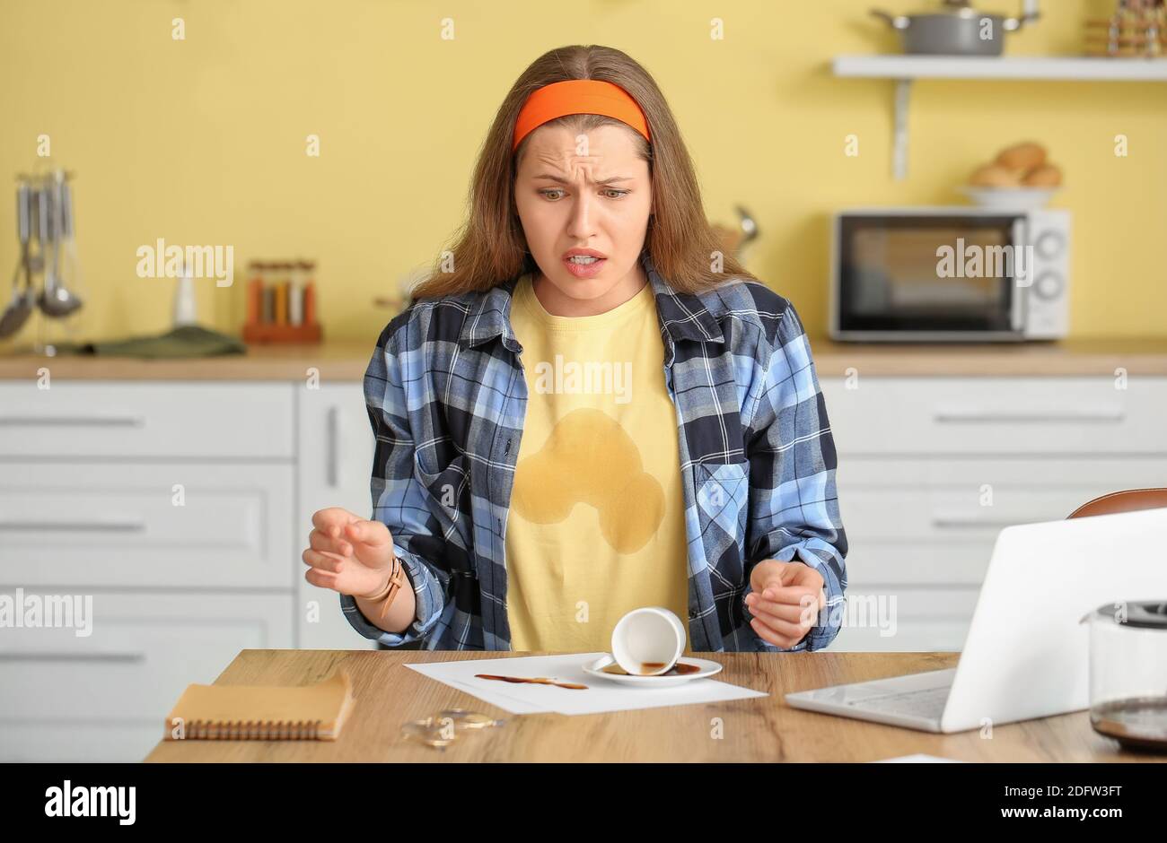Gestresste junge Frau mit Kaffeeflecken auf ihrem T-Shirt und Verschütteter Kaffee in der Küche Stockfoto