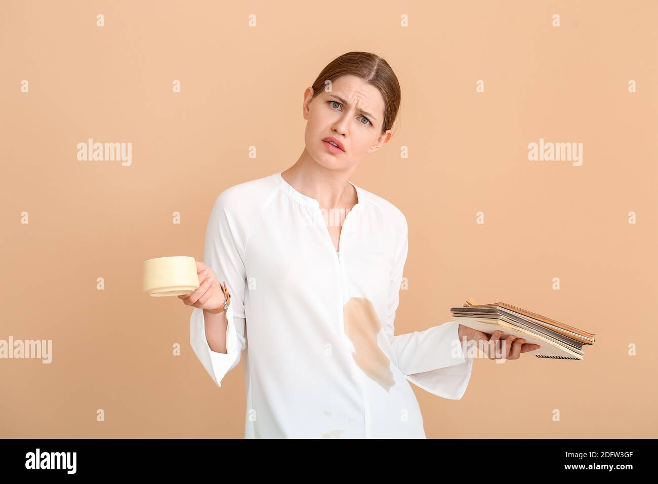 Gestresste junge Frau mit Kaffeeflecken auf ihrem Hemd Farbiger Hintergrund Stockfoto