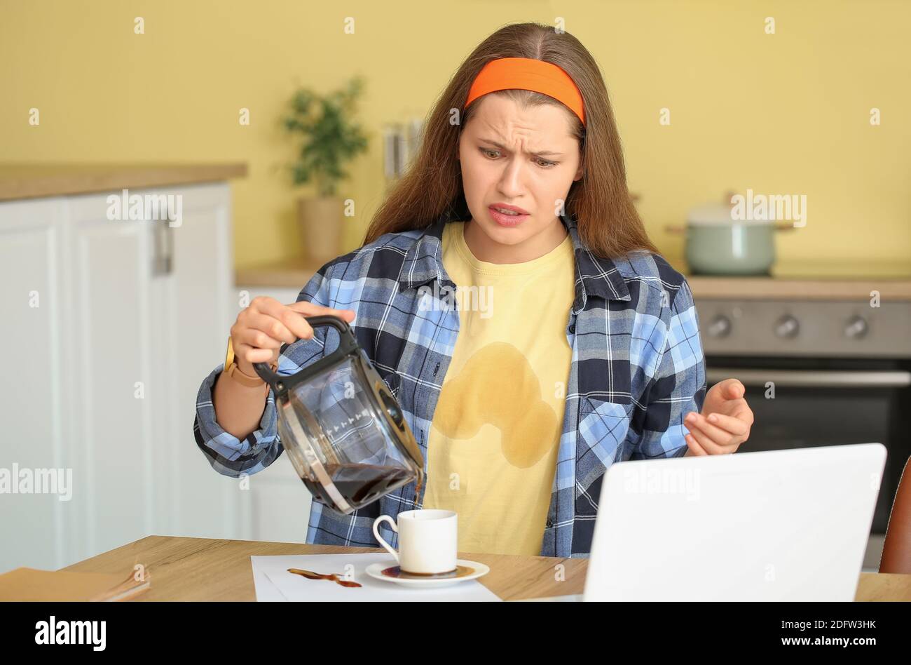Gestresste junge Frau mit Kaffeeflecken auf ihrem T-Shirt und Verschütteter Kaffee in der Küche Stockfoto