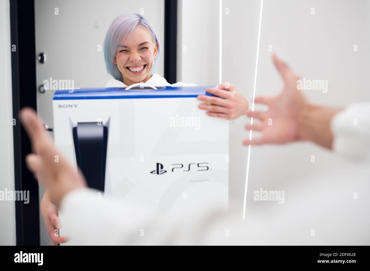 Mädchen hat gerade ein Delivery von einem neuen PlayStation 5 Gaming-Konsole und überraschen ihren Freund mit einem Geschenk an Spielen Sie zusammen auf einer Selbstisolation auf Stockfoto