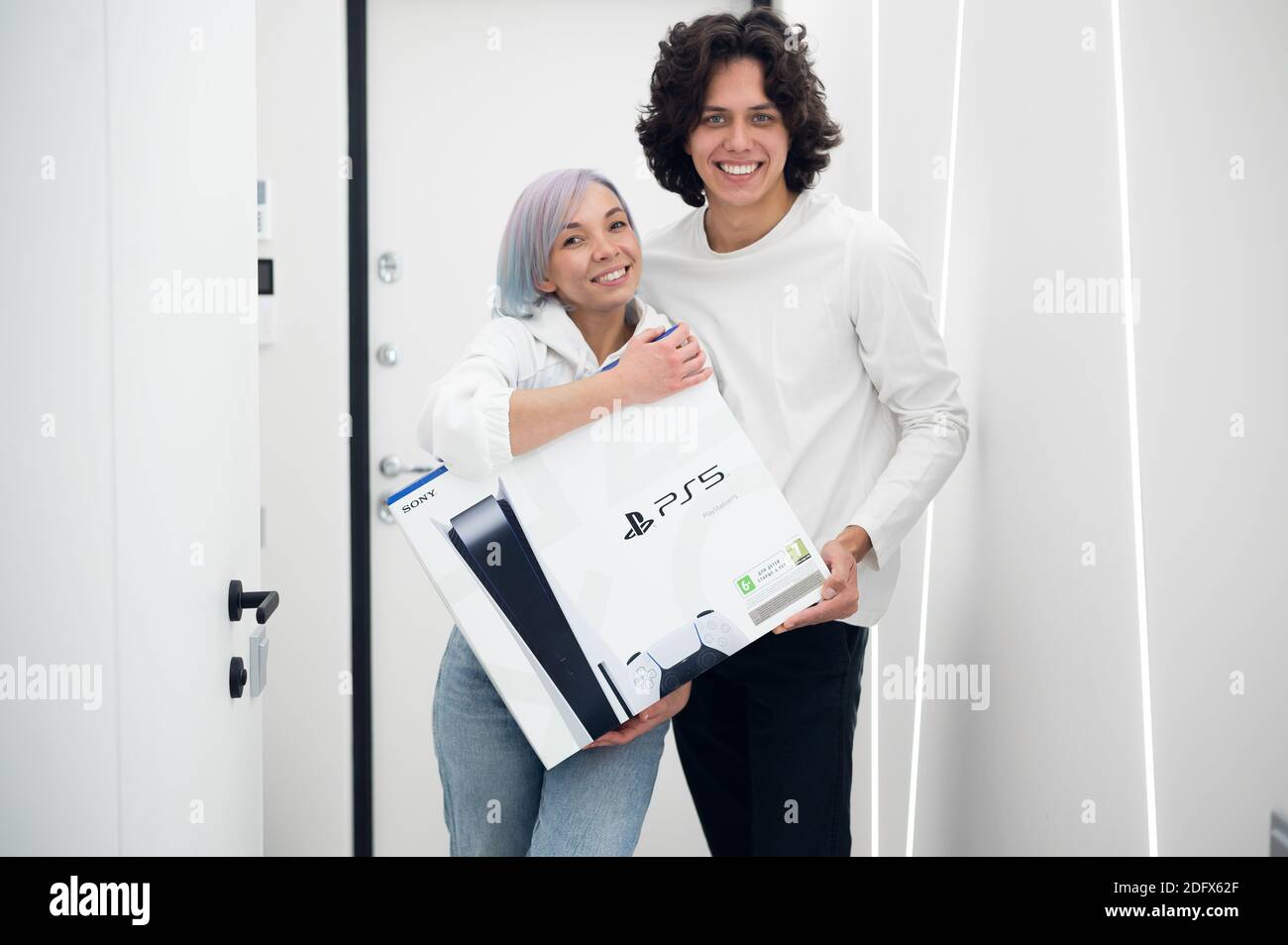 Ein glückliches junges Paar ist gerade mit einer brandneuen PlayStation 5-Spielekonsole von Sony aus dem Geschäft nach Hause gekommen. Sie haben es bei einem Black Friday-Verkauf bekommen. Moskau - November Stockfoto