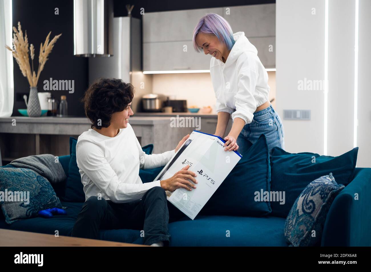 Mädchen hat gerade ein Delivery von einem neuen PlayStation 5 Gaming-Konsole und überraschen ihren Freund mit einem Geschenk an Spielen Sie zusammen auf einer Selbstisolation auf Stockfoto