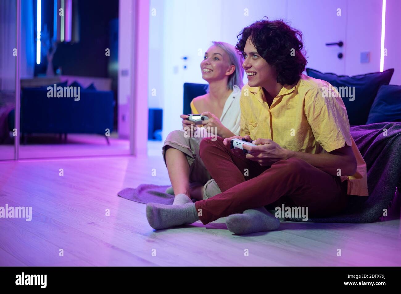 Ein paar junge Erwachsene spielen Videospiele zu Hause. Emotionale diverse Gamer halten Joysticks und konkurrieren in intensiven Videospiel auf Spielkonsole. Stockfoto