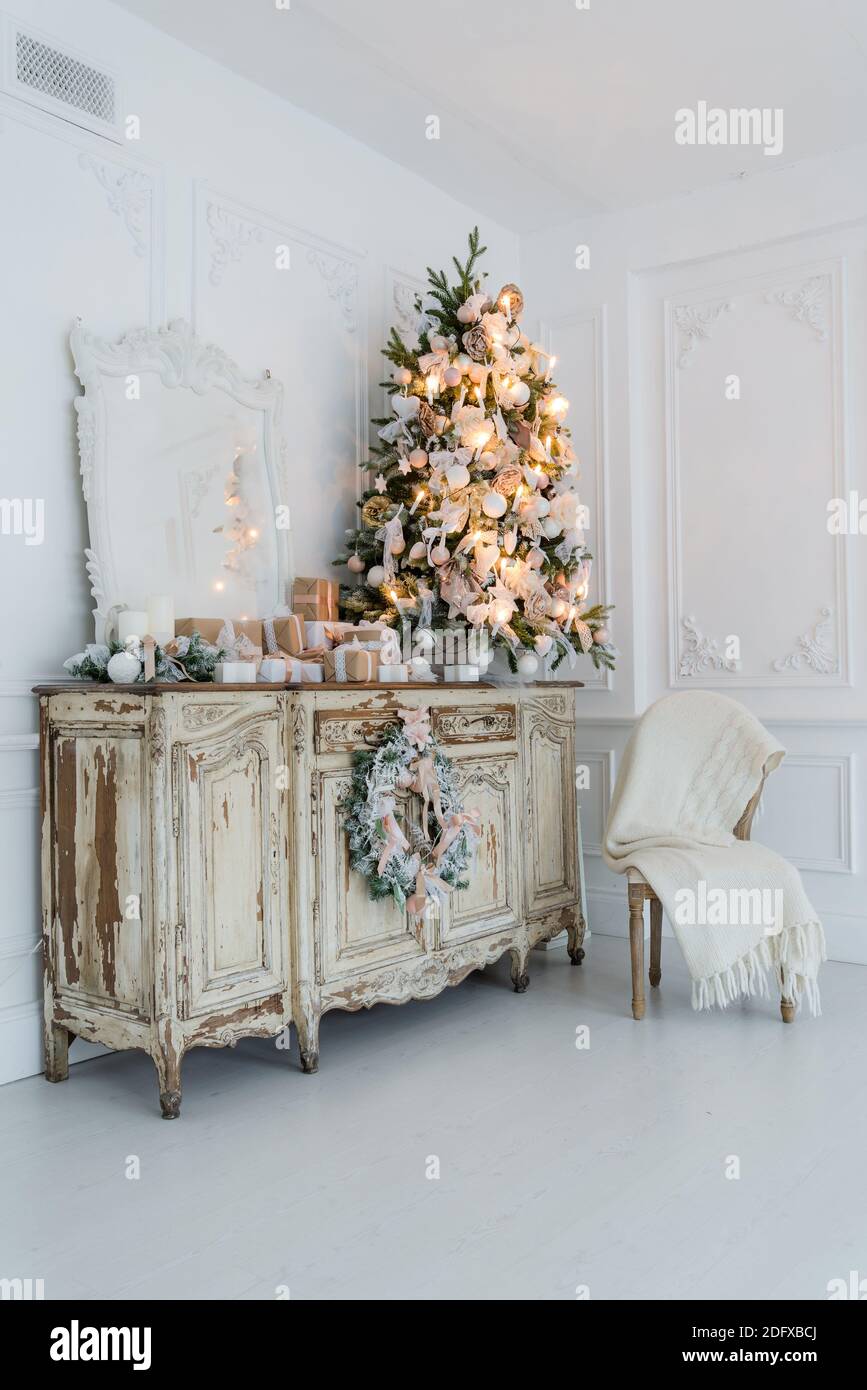 Geschmückter Weihnachtsbaum auf hölzerne Kommode Kommode Kommode in weiße Interieur mit künstlichen Blumen, Girlanden und Spielzeug Stockfotografie