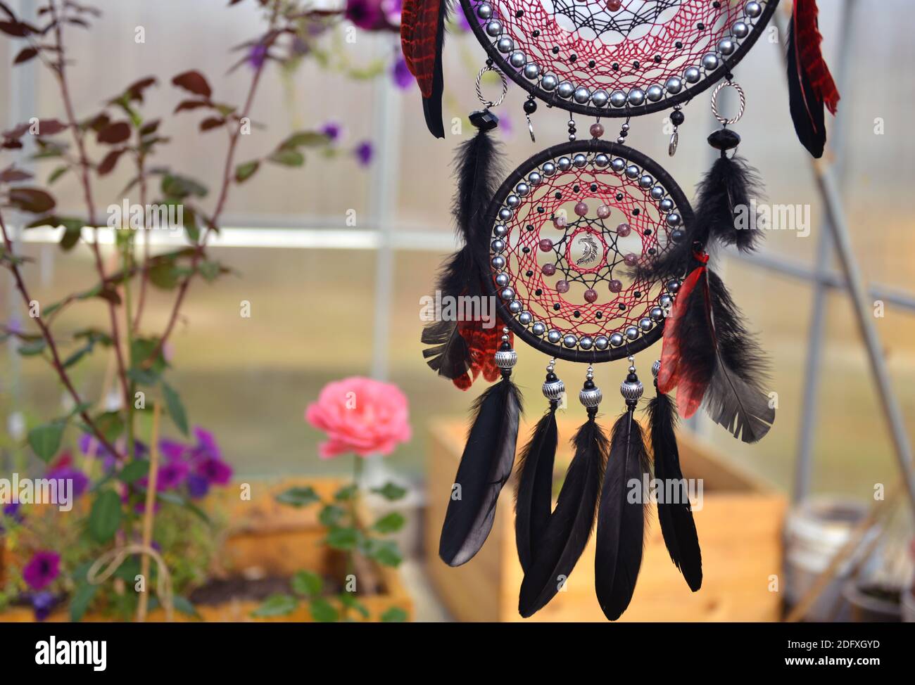 Schöner boho-roter und schwarzer Traumfänger mit Federn im Zigeunerstil. Mystischer natürlicher Hintergrund mit Traumfänger, esoterischem und okkulten Konzept Stockfoto