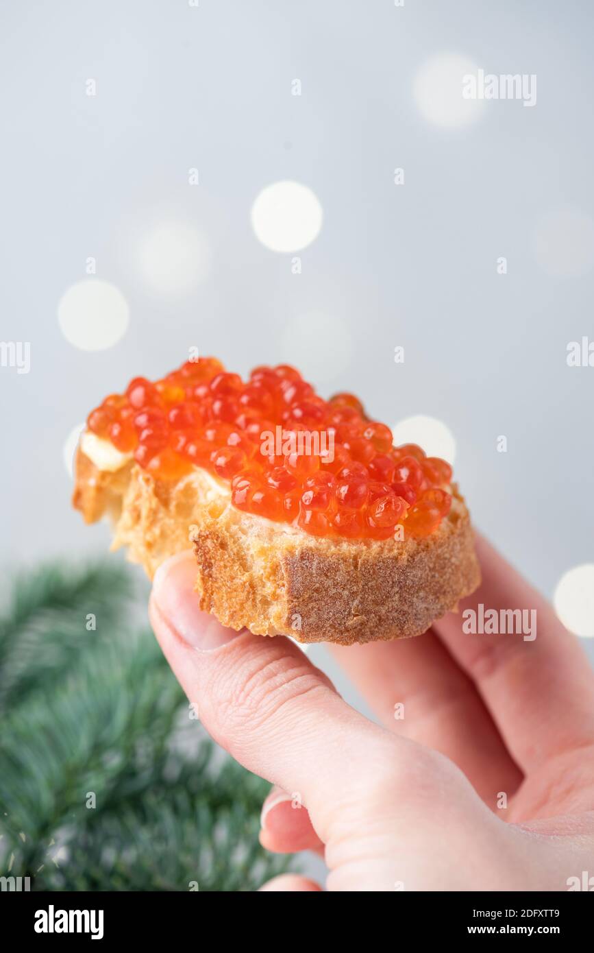 Weibliche Hand hält Luxus-Canape mit rotem Kaviar und Butter. Weihnachten, Neujahr russische Vorspeise Essen Stockfoto