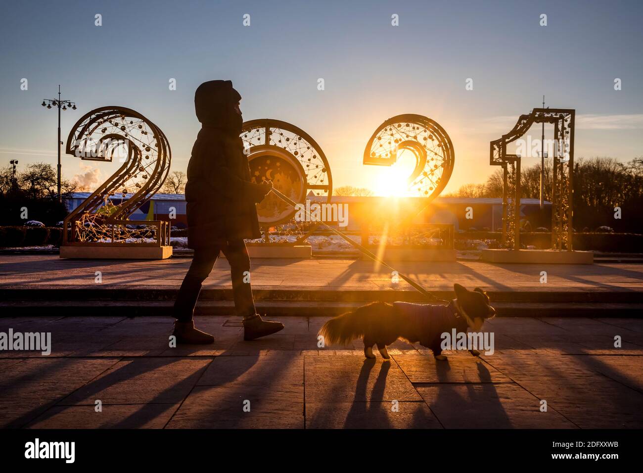 Moskau, Russland. 6. Dezember 2020 EINE Frau geht mit ihrem Hund vor den Hintergrund der Jahreszahlen "2021", die im Gorki-Park in Moskau, Russland, spielt Stockfoto