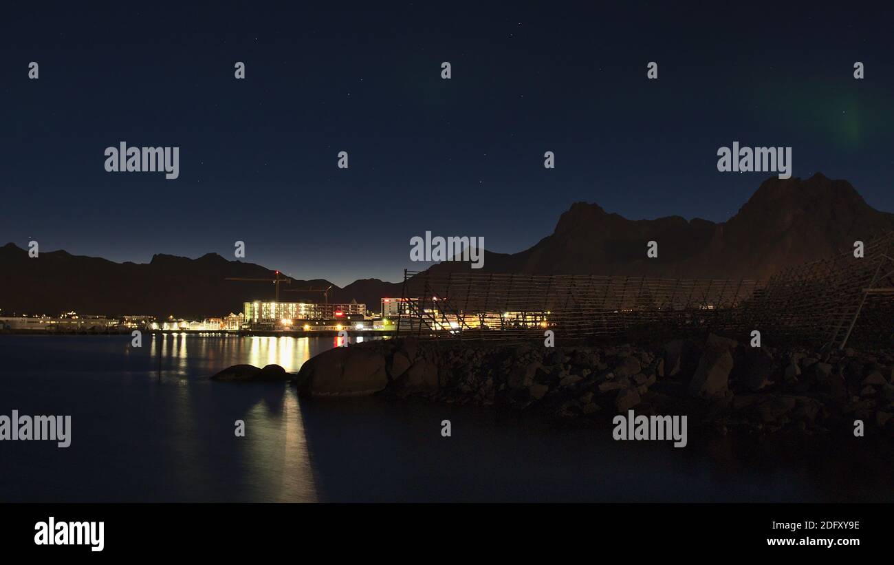 Schöne Nacht Blick auf die Küste der Insel Austvågøya, Lofoten, Norwegen mit traditionellen Stockfisch Trockenracks und beleuchteten Stadt Svolvær. Stockfoto