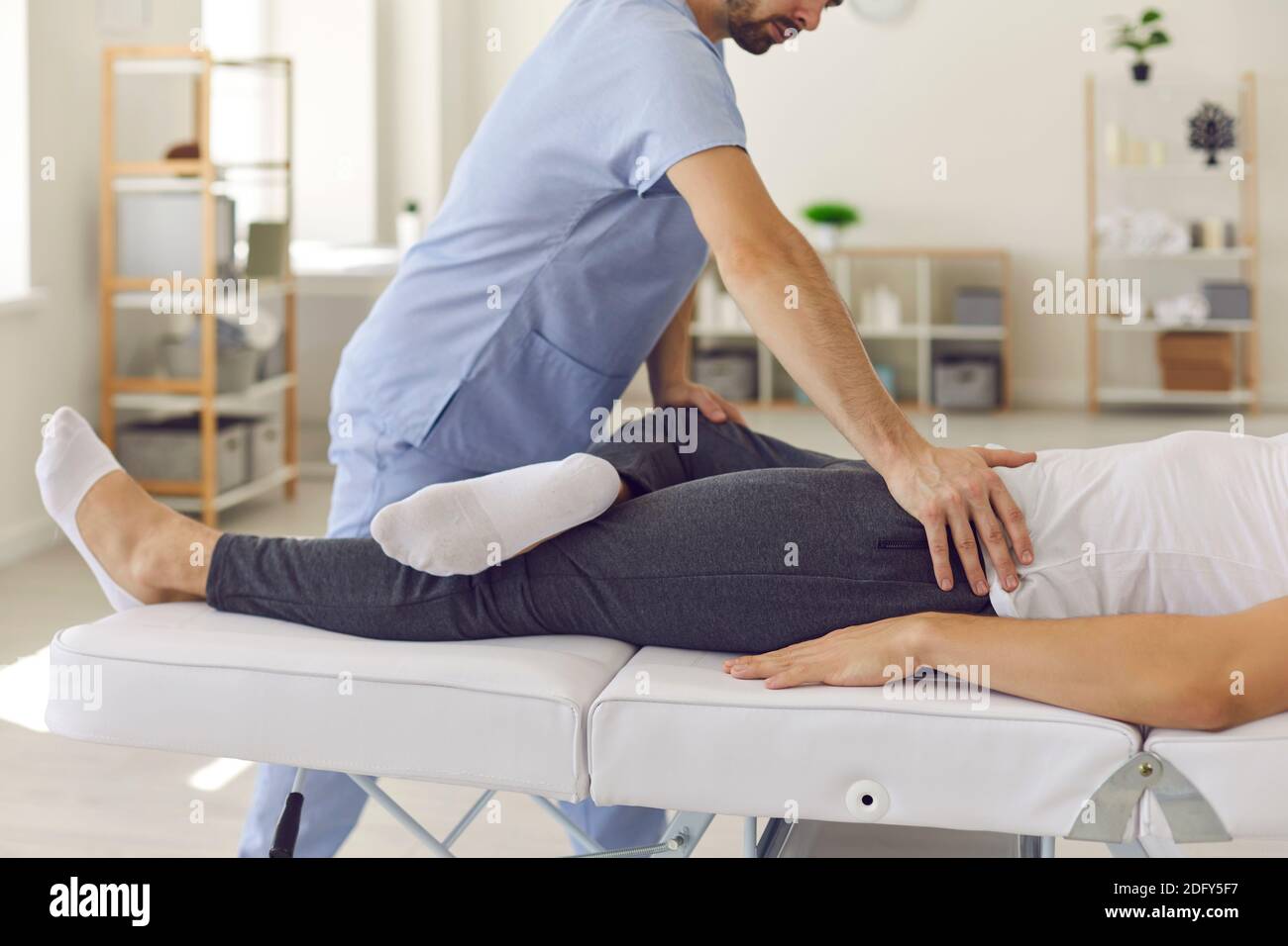 Selbstbewusster Mann professioneller Arzt Osteopath Fixierung Mann patinets Beine in Position zum Fixieren von Verbindungen Stockfoto