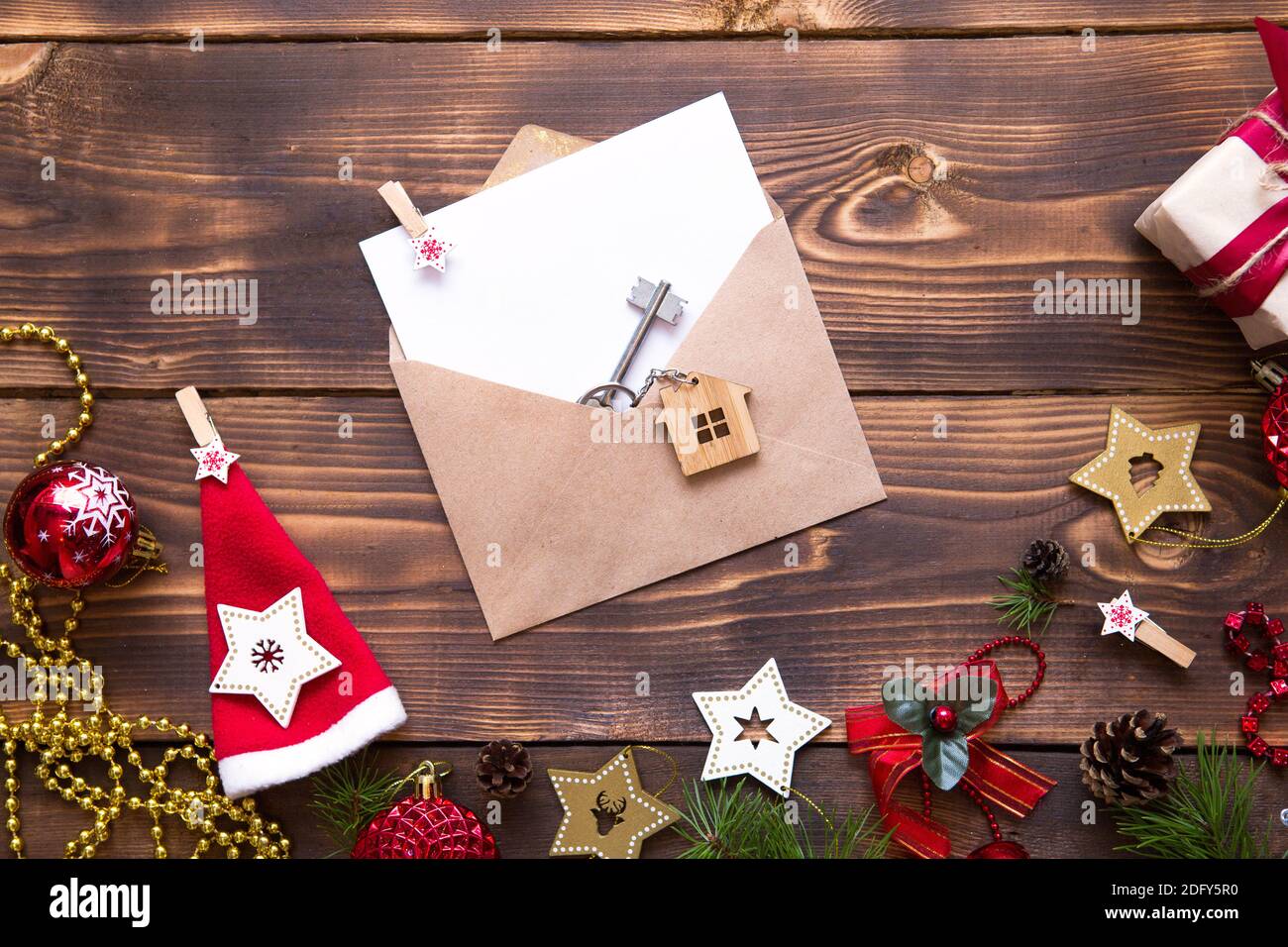 Weihnachtswohnung lag auf einem hölzernen Hintergrund mit Schlüsseln zu neuem Haus in der Mitte mit einem Umschlag mit einem Zettel. Neues Jahr, Übertragung, Aktien der Mo Stockfoto