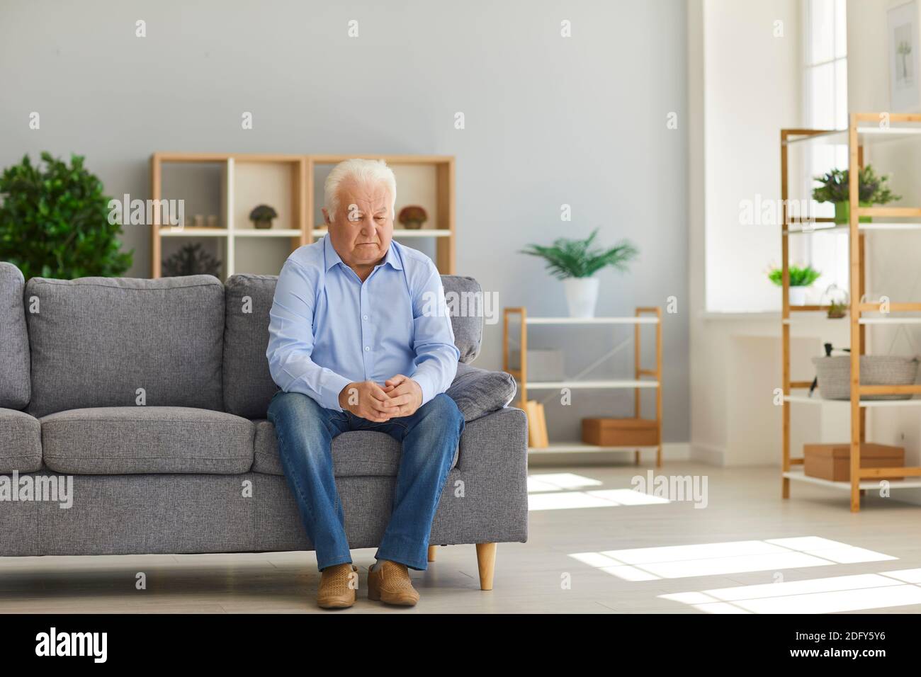 Älterer Mann sitzt zu Hause auf dem Sofa und fühlt sich deprimiert, einsam und von seiner Familie verlassen Stockfoto