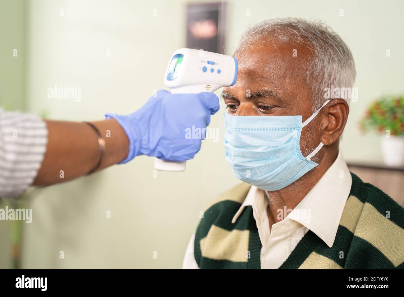 Nahaufnahme der Hände des Arztes, die die Temperatur der alten Kranken überprüfen Mann mit Infrarot-Thermometer im Krankenhaus, während beide Gesicht getragen Maske durch Coronavirus covi Stockfoto
