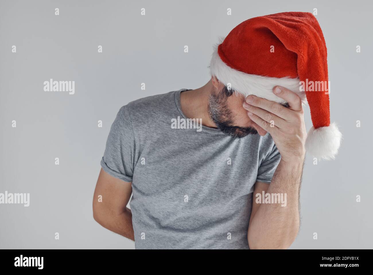 Weihnachten Urlaub Depression, traurig schmollenden Mann mit Weihnachtsmann Hut bedeckt Gesicht mit den Händen und weint allein in der Zeit der Traurigkeit, Selbstreflexion, Stockfoto