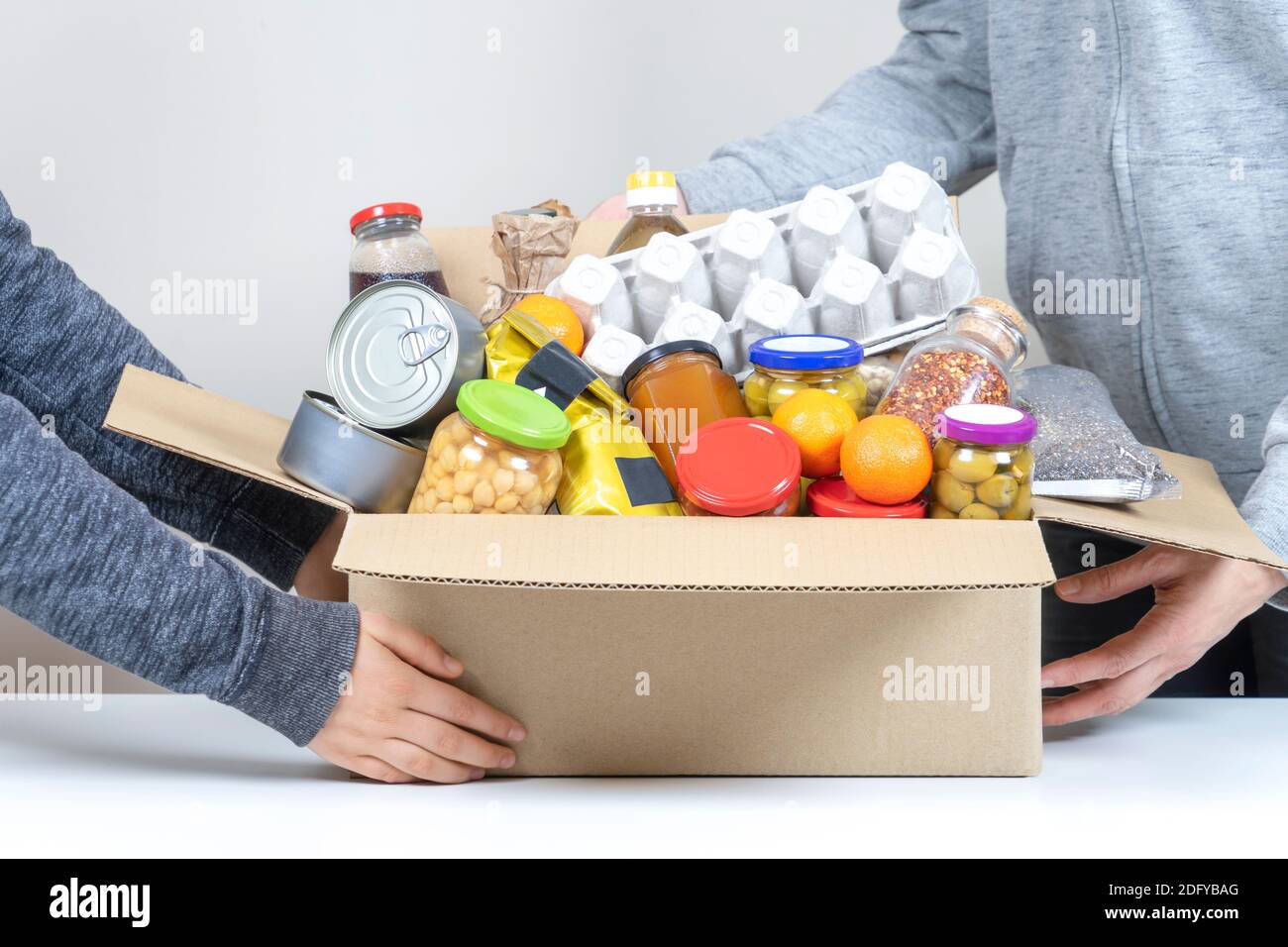 Freiwillige Hände halten Lebensmittel Spenden Box mit Lebensmitteln auf Weißer Schreibtisch Stockfoto