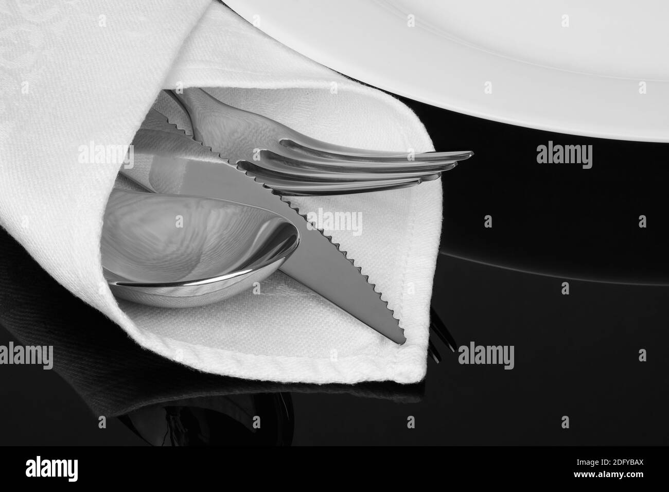 Nahaufnahme von Messer, Gabel und Löffel mit weißer Leinenserviette auf schwarzem Hintergrund. Stockfoto