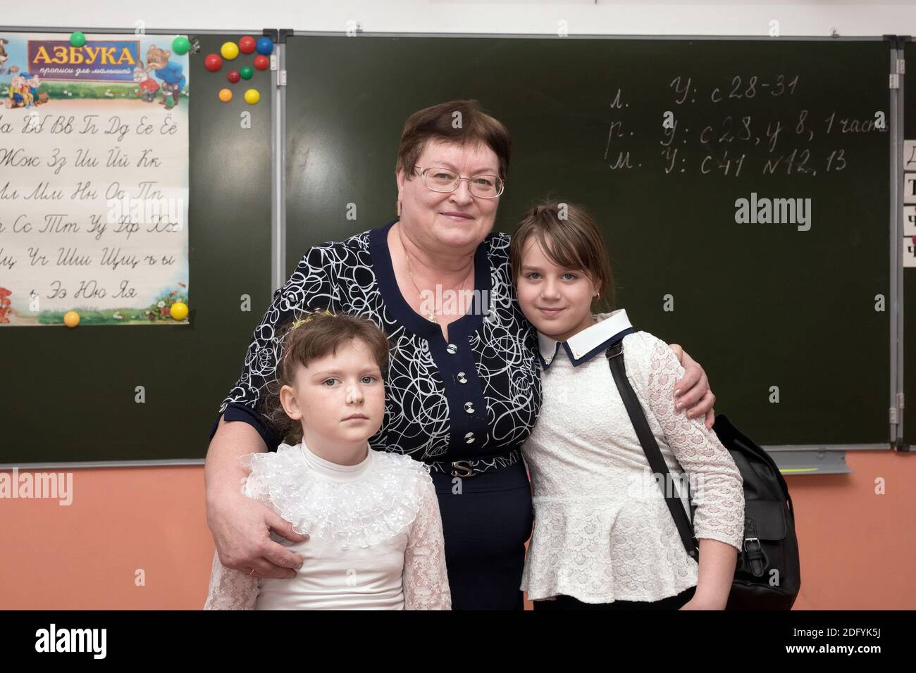 Der Lehrer steht mit den Erstklässlern vor dem Hintergrund der Tafel mit dem russischen Alphabet im Klassenzimmer. Stockfoto