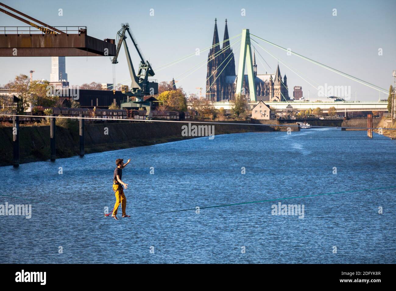 Mann auf Slackline im Rheinhafen im Stadtteil Deutz, im Hintergrund Dom und Severins Brücke, Köln, Deutschland. Stockfoto