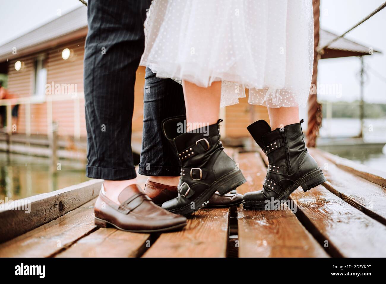Beine der gerade verheirateten auf dem Hintergrund der Werft.die Braut und Bräutigam stehen und posieren in Stiefeln auf dem Pier. Stockfoto