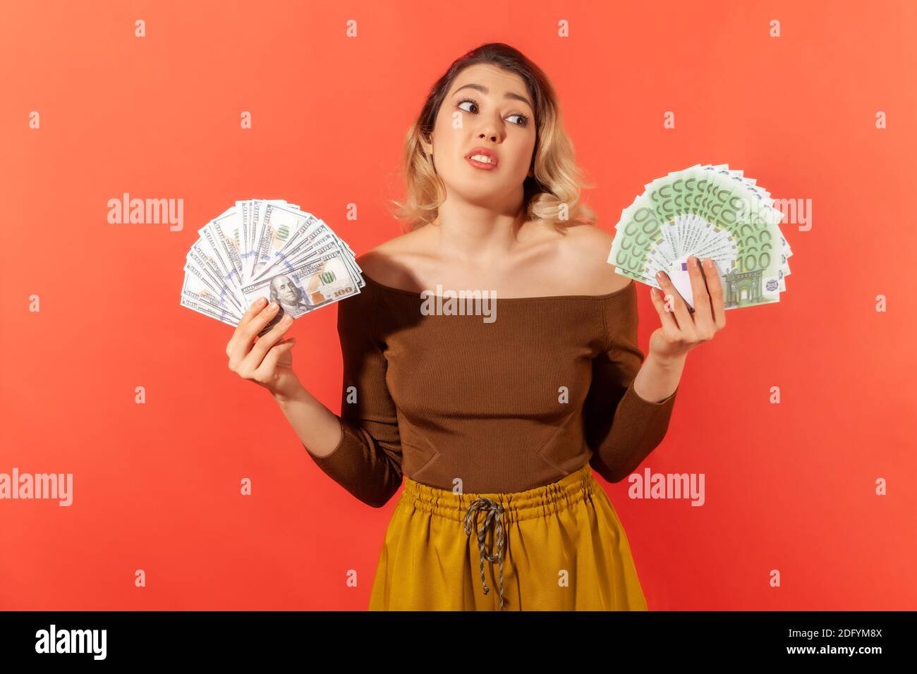 Überrascht merkantile Frau hält Fans von Dollar und Euro-Banknoten, Wechselkurse, Zahlungsdienst. Innenaufnahme des Studios isoliert auf Orange Stockfoto