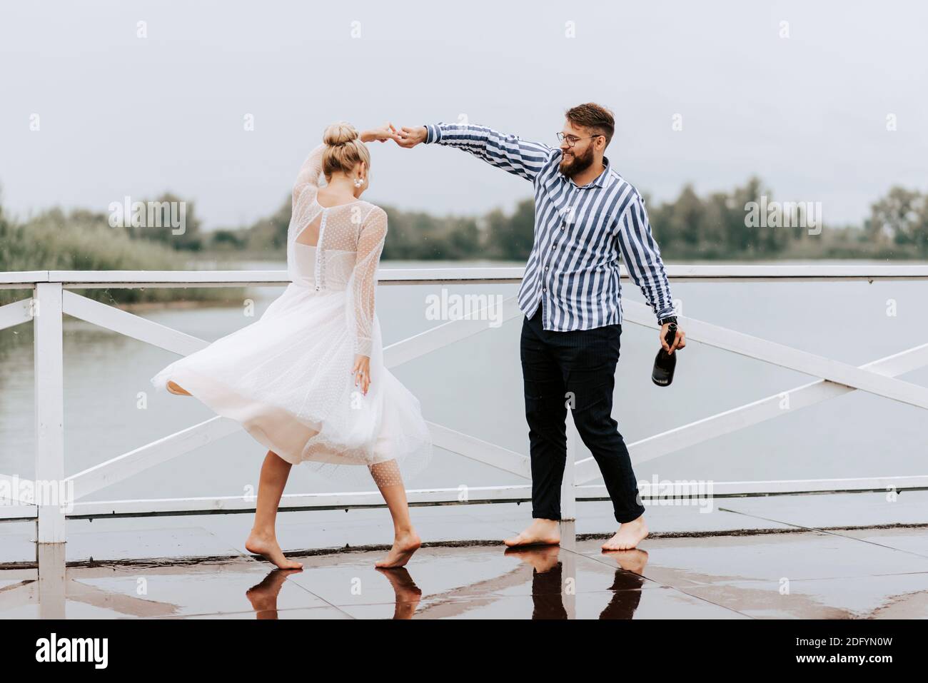 Ein Mann und eine Frau tanzen barfuß und haben Spaß auf dem Kai am See. Stockfoto