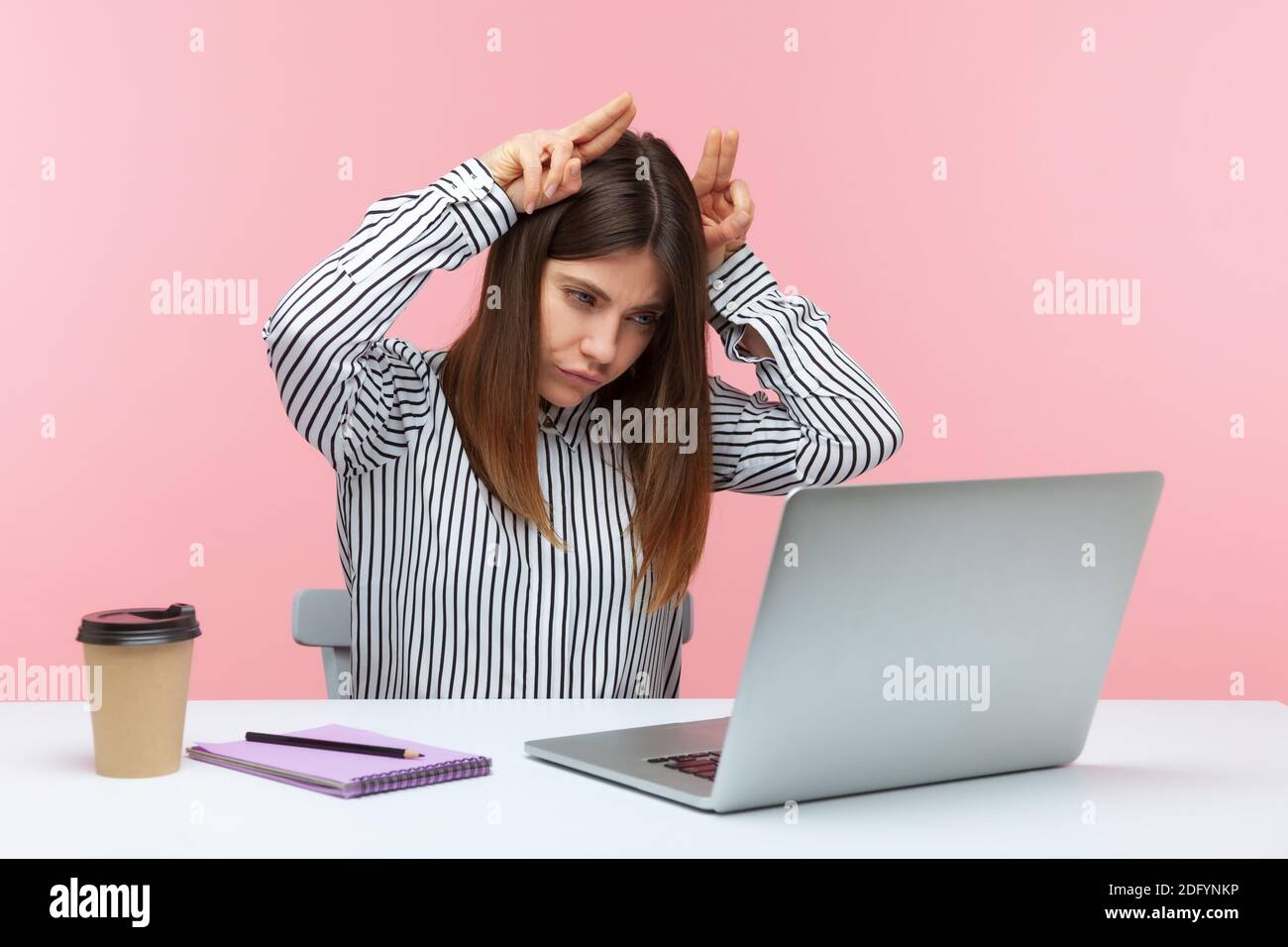 Aggressive Geschäftsfrau hält die Finger über dem Kopf tun Bullhorn Geste und Blick auf Laptop-Bildschirm mit Wut, drohende sprechen auf Video cal Stockfoto