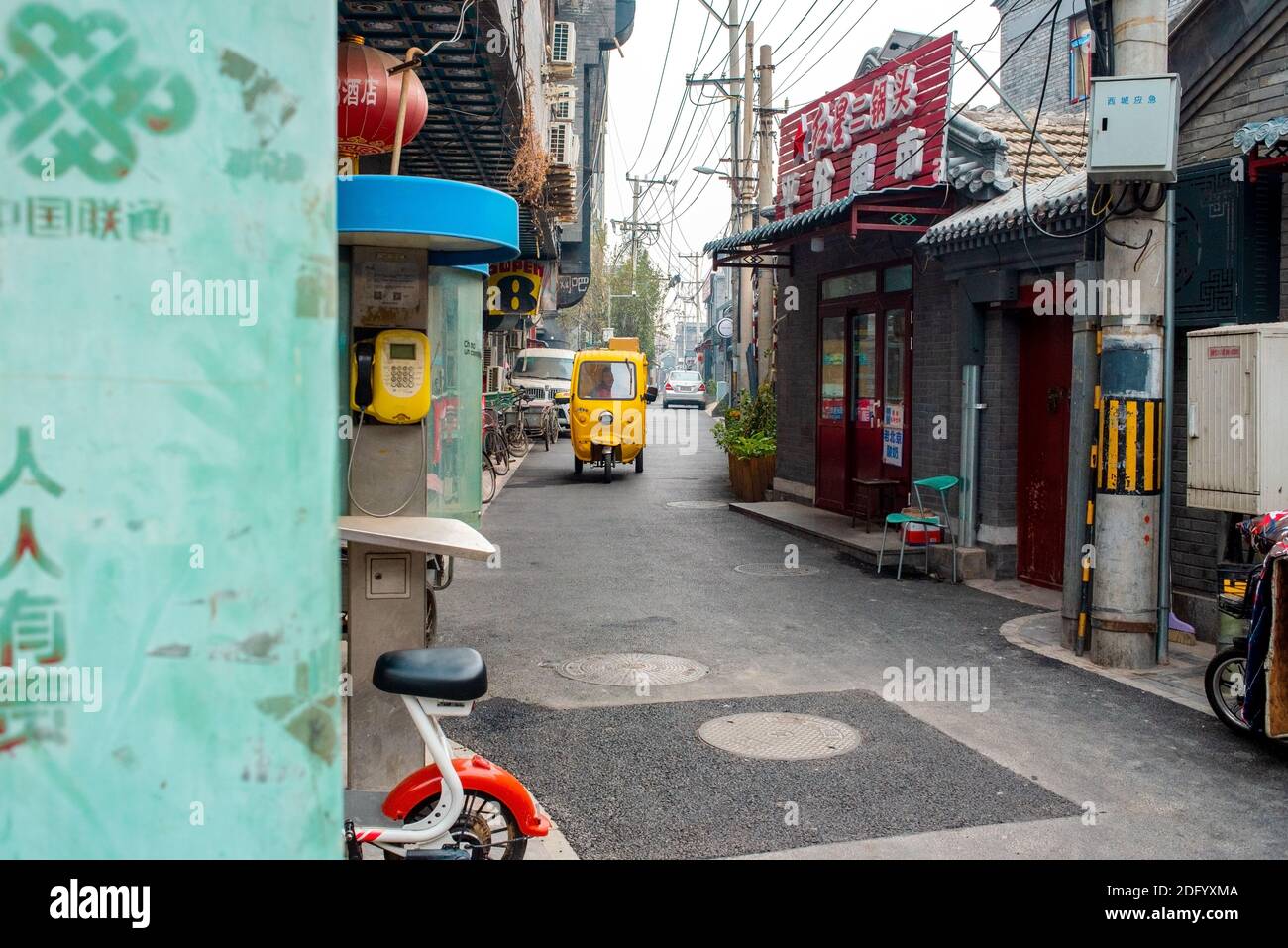 Gelbe Auto-Rikscha fährt entlang einer Straße im historischen Hutong-Viertel. Hutong ist eine Art von engen Straßen oder Gassen, die häufig mit Peking verbunden sind. Stockfoto