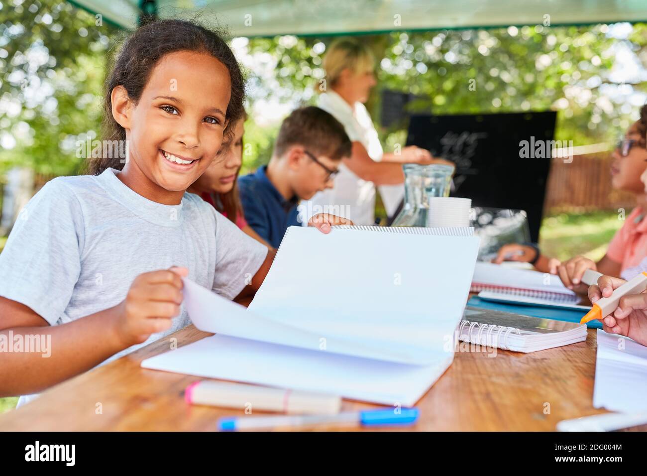 Glückliches Mädchen mit Übungsbuch studiert in der Sommerschule Sommer Nachhilfekurs Stockfoto