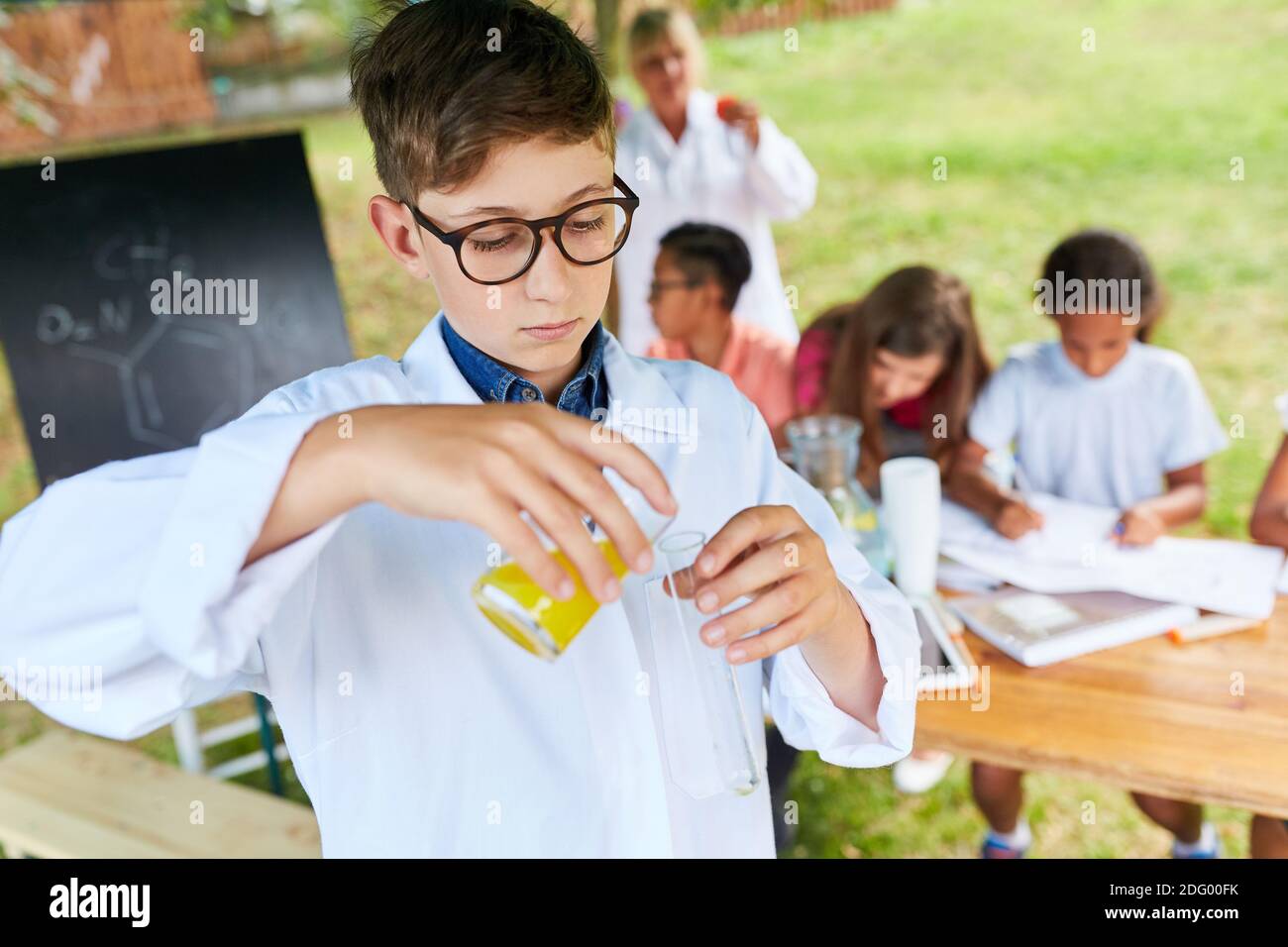 Kind im weißen Mantel, das ein Laborexperiment mit Reagenzien macht In der Chemie Sommerschule Stockfoto