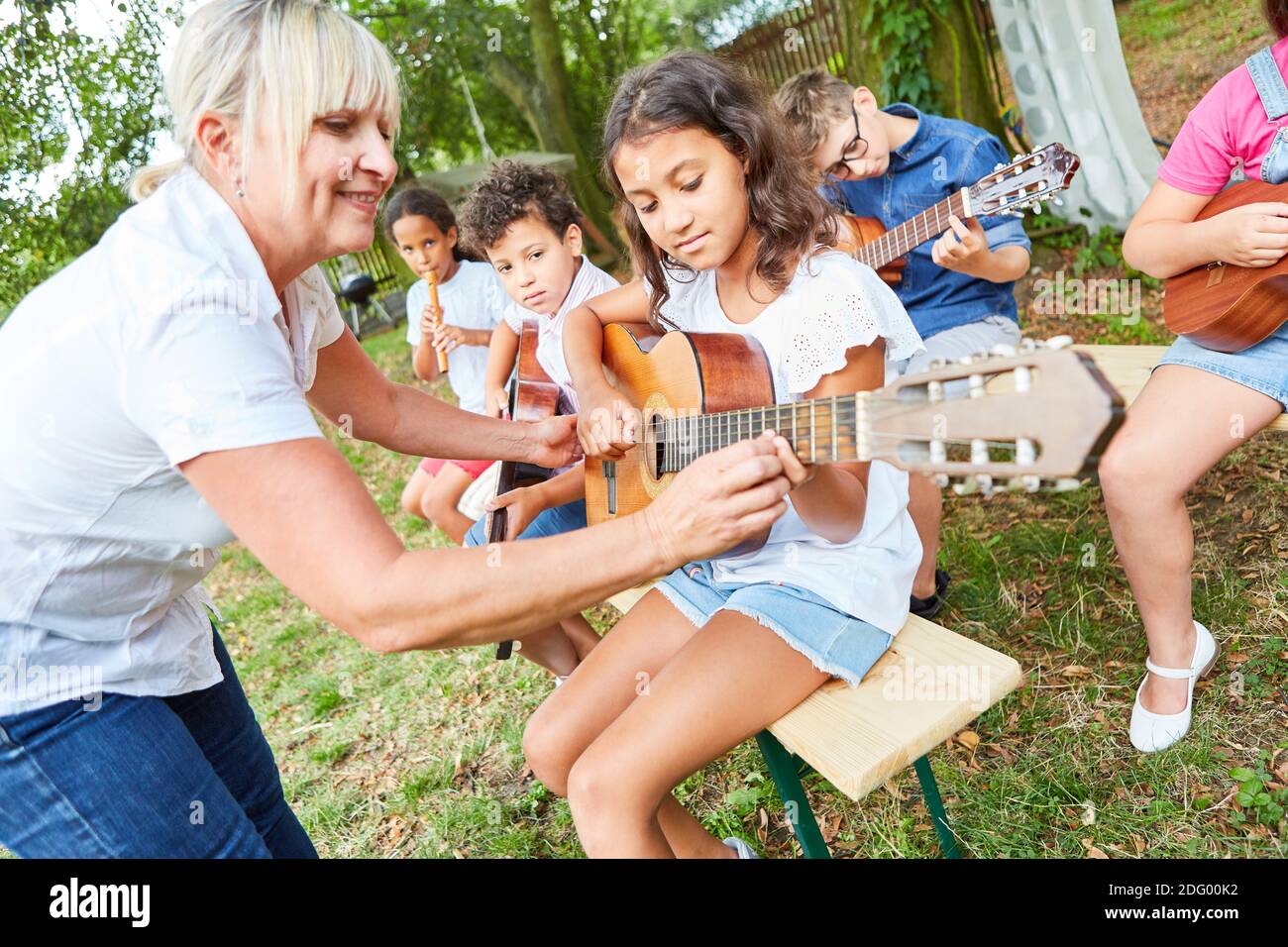 Lehrer hilft Kindern, Gitarre in der Klasse zu spielen Sommercamp oder Sommercamp Stockfoto