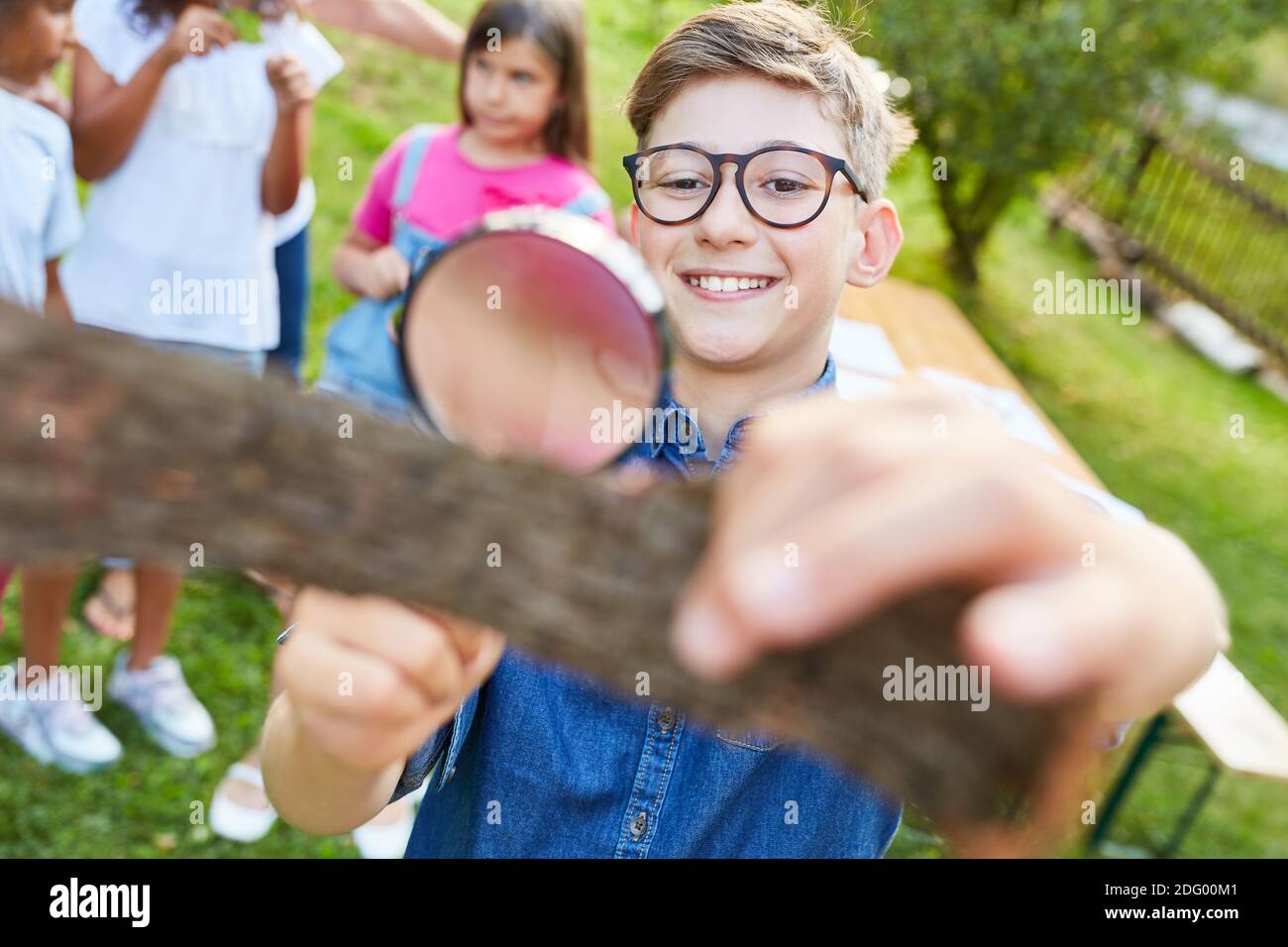 Kinder schauen neugierig auf Baumrinde durch ein Vergrößerungsglas Im ökologischen Ferienlager Stockfoto